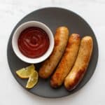 Air fried brats and ketchup on a plate.