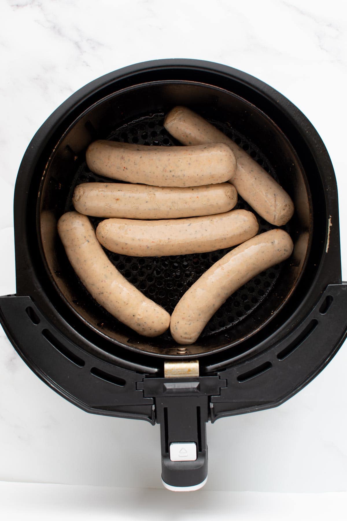 Uncooked brats in an air fryer.