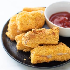 Homemade fish sticks on a plate with ketchup on the side.