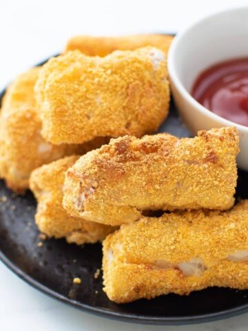 Homemade fish sticks on a plate with ketchup on the side.