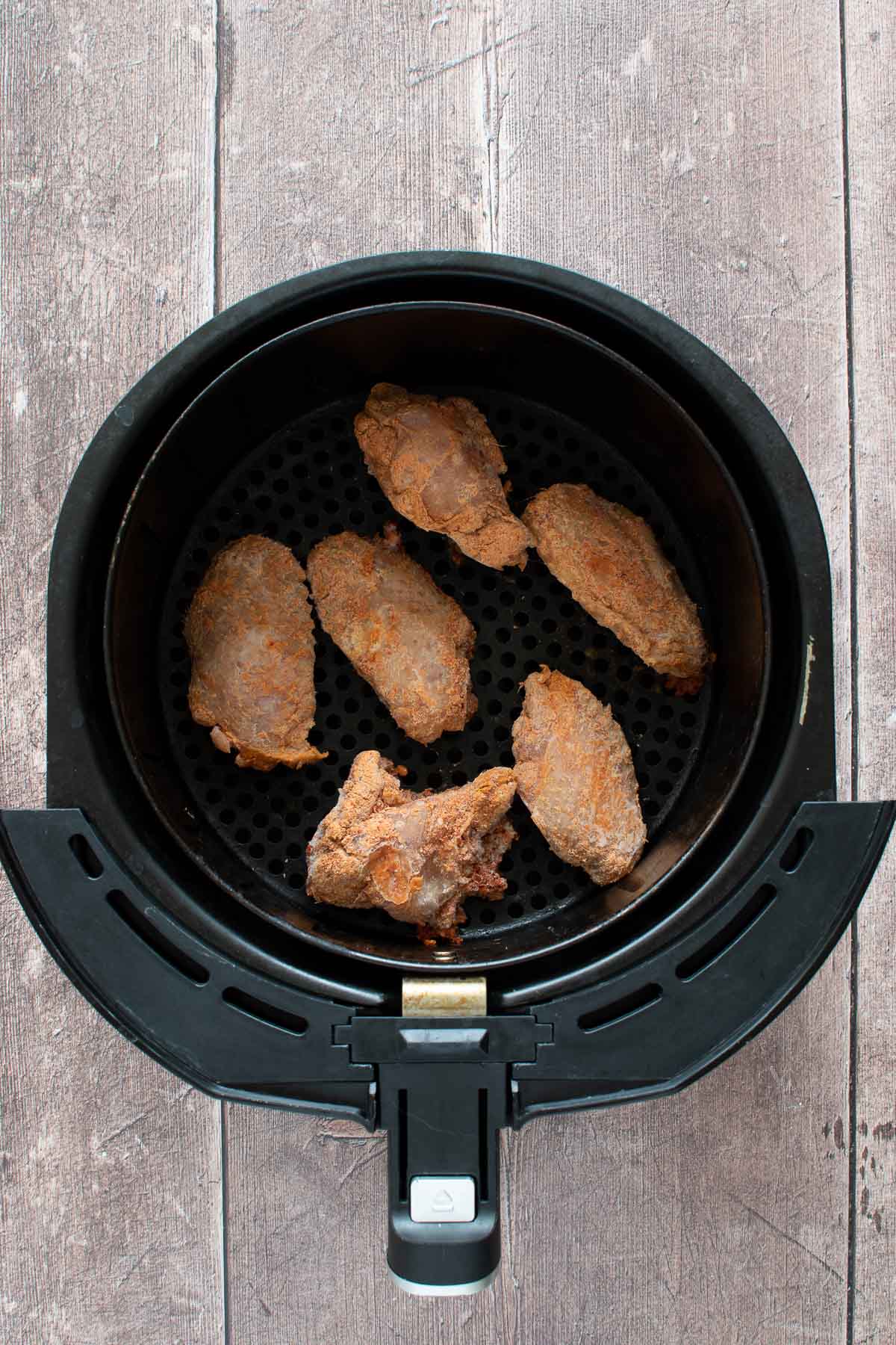 Frozen chicken wings in an air fryer.