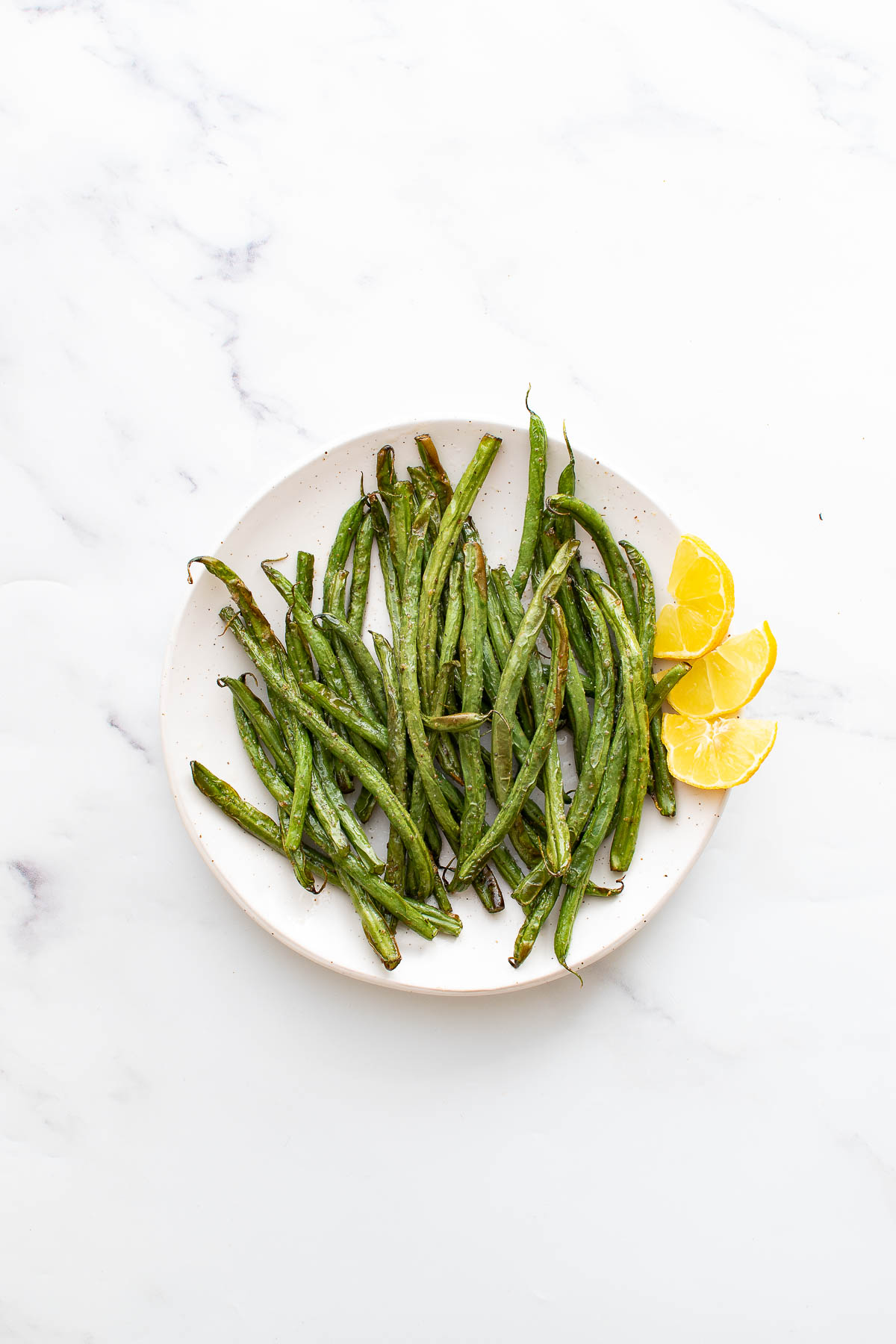 Air fried green beans on a plate with lemon wedges.