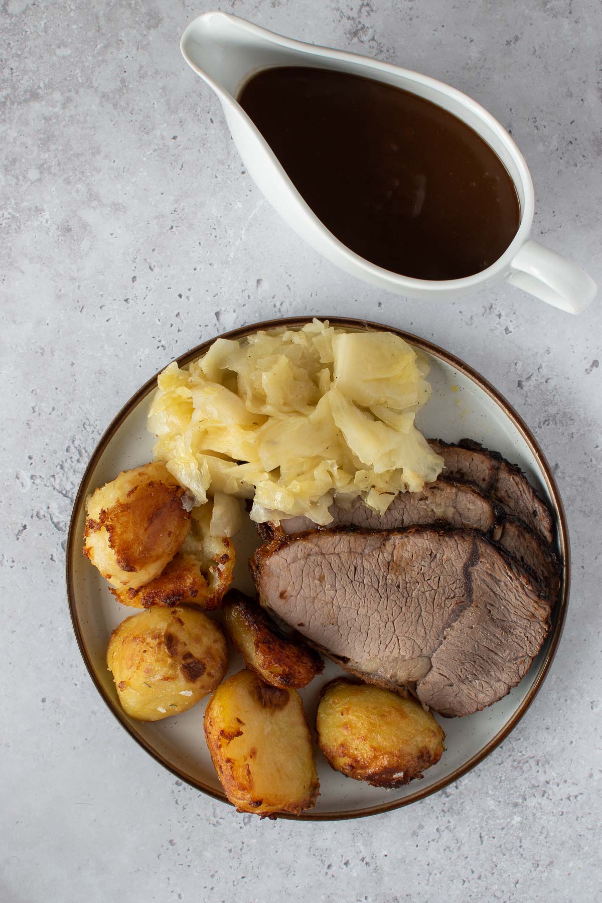 A plate with roast beef, cabbage and roasted potatoes, with gravy on the side.