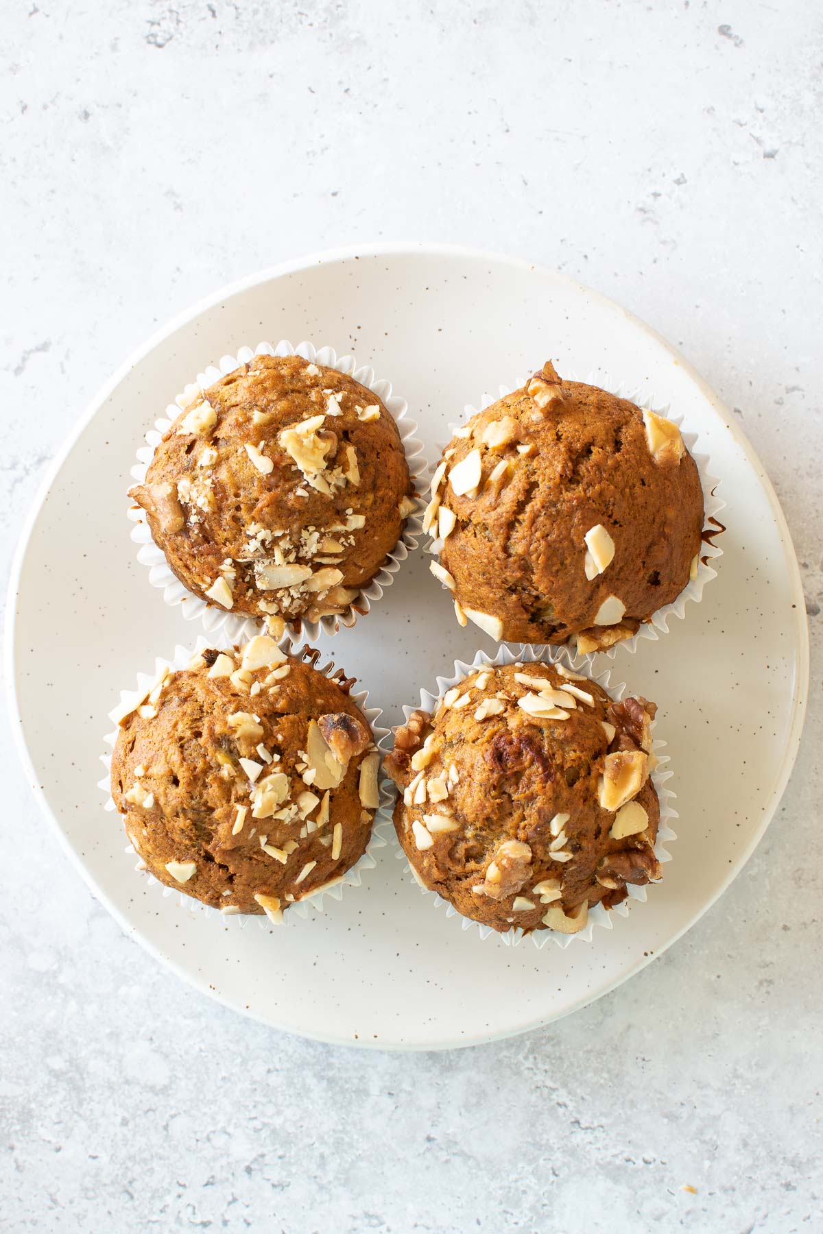 Four muffins with banana and carrots on a plate.