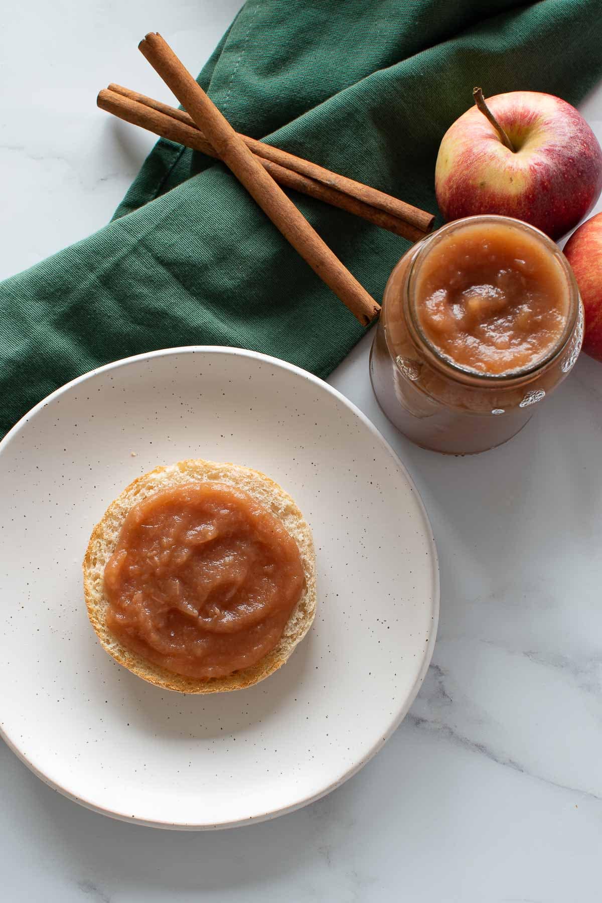 English muffin with apple butter, with a jar of apple butter on the side.