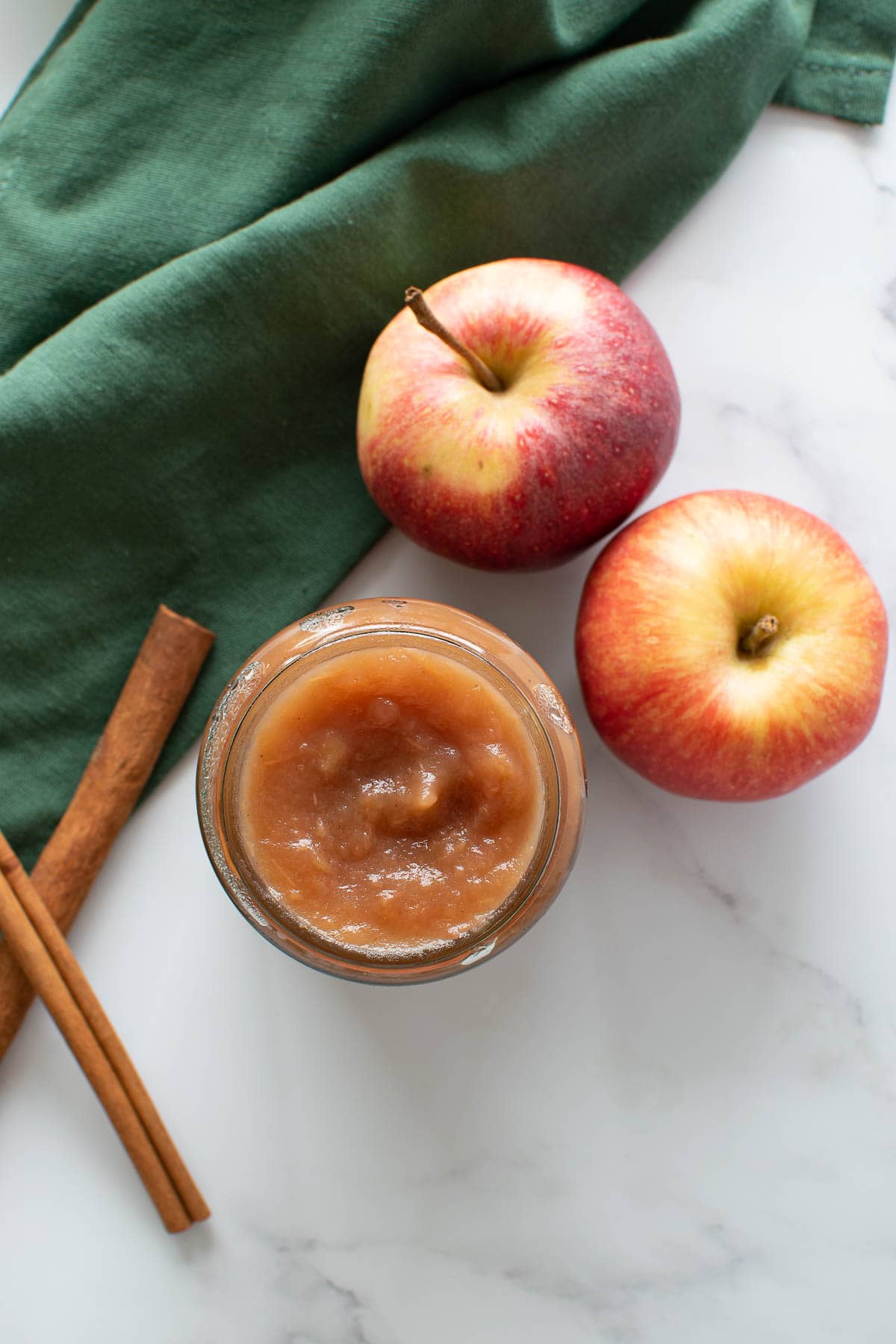 Apple butter in a mason jar, with apples and cinnamon sticks on the side.