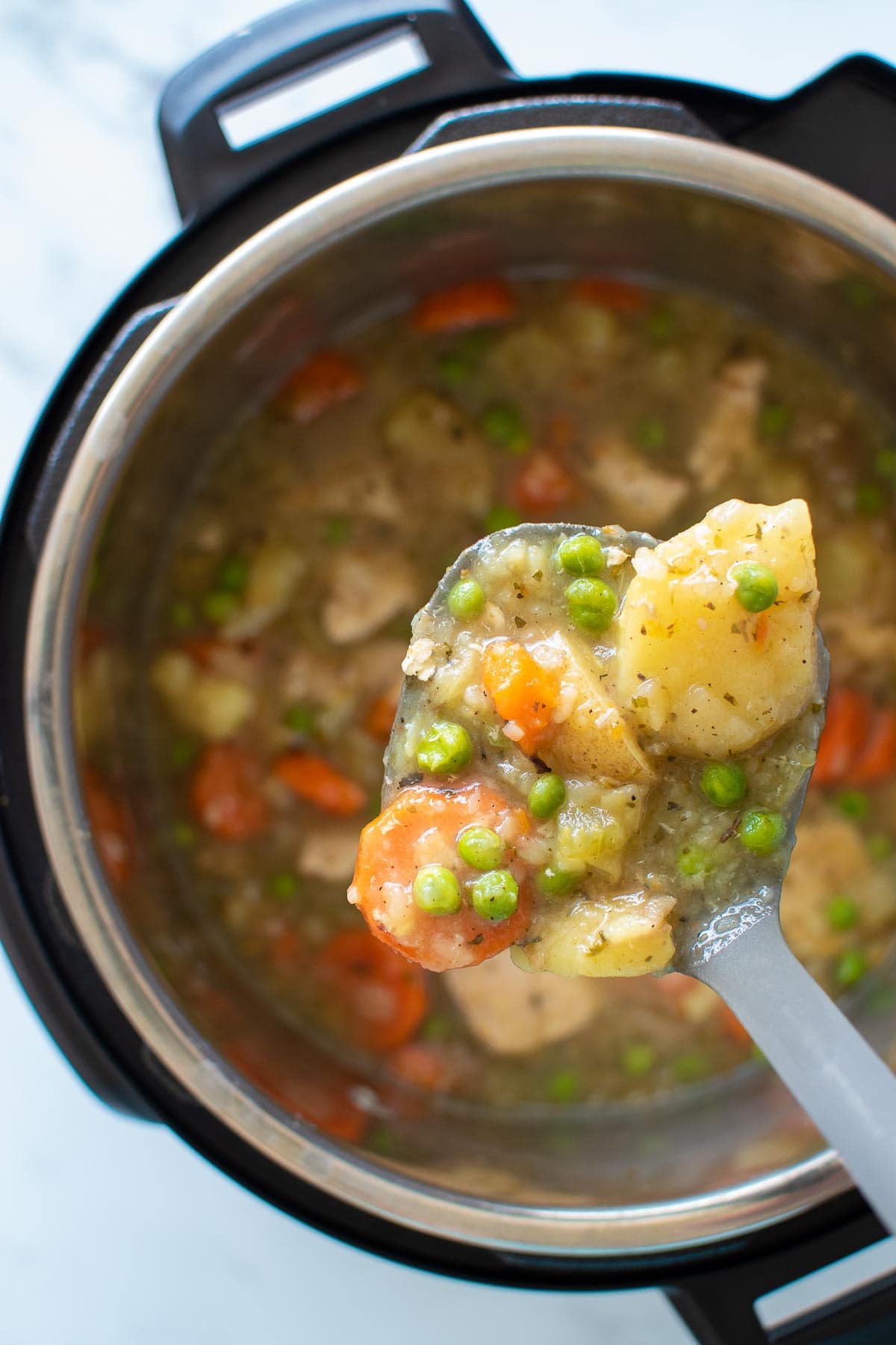 A ladle filled with chicken stew from an Instant Pot.