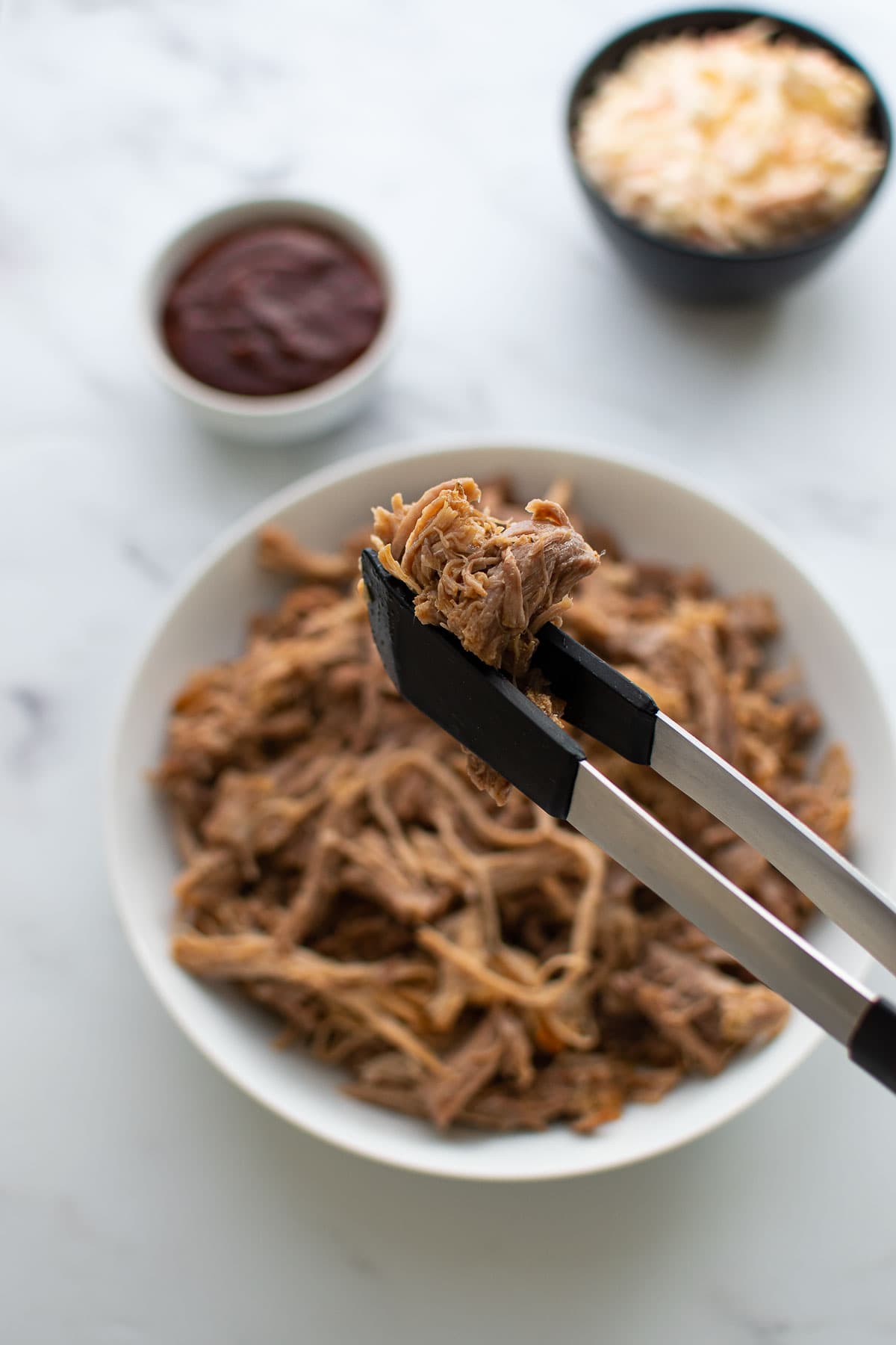 Tongs picking up a serving of pulled pork.