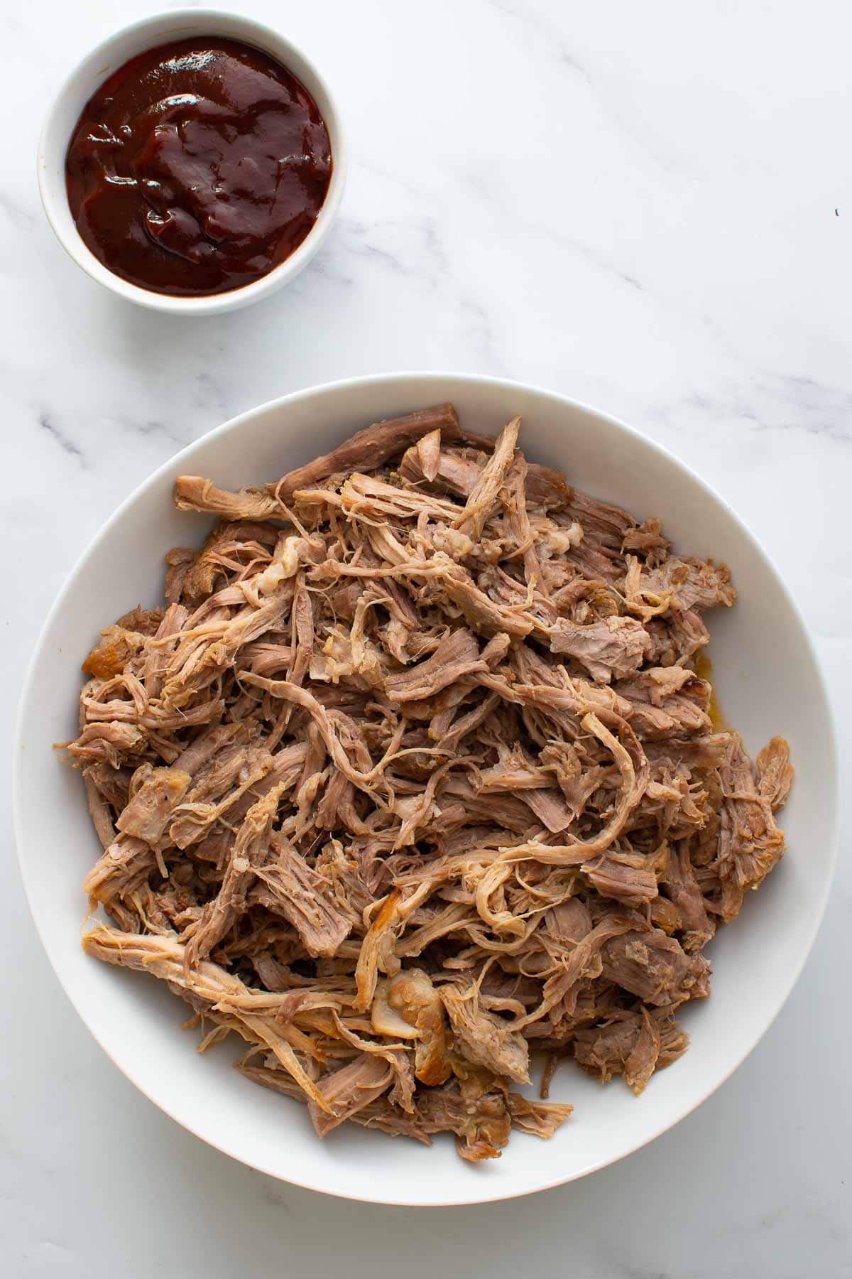 Pulled pork in a bowl with bbq sauce on the side.