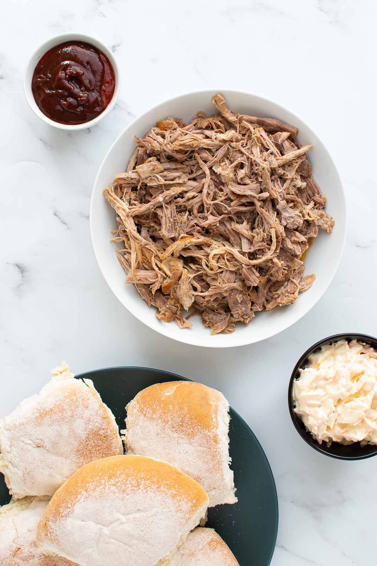 Pulled pork, rolls, bbq sauce and coleslaw on a table.