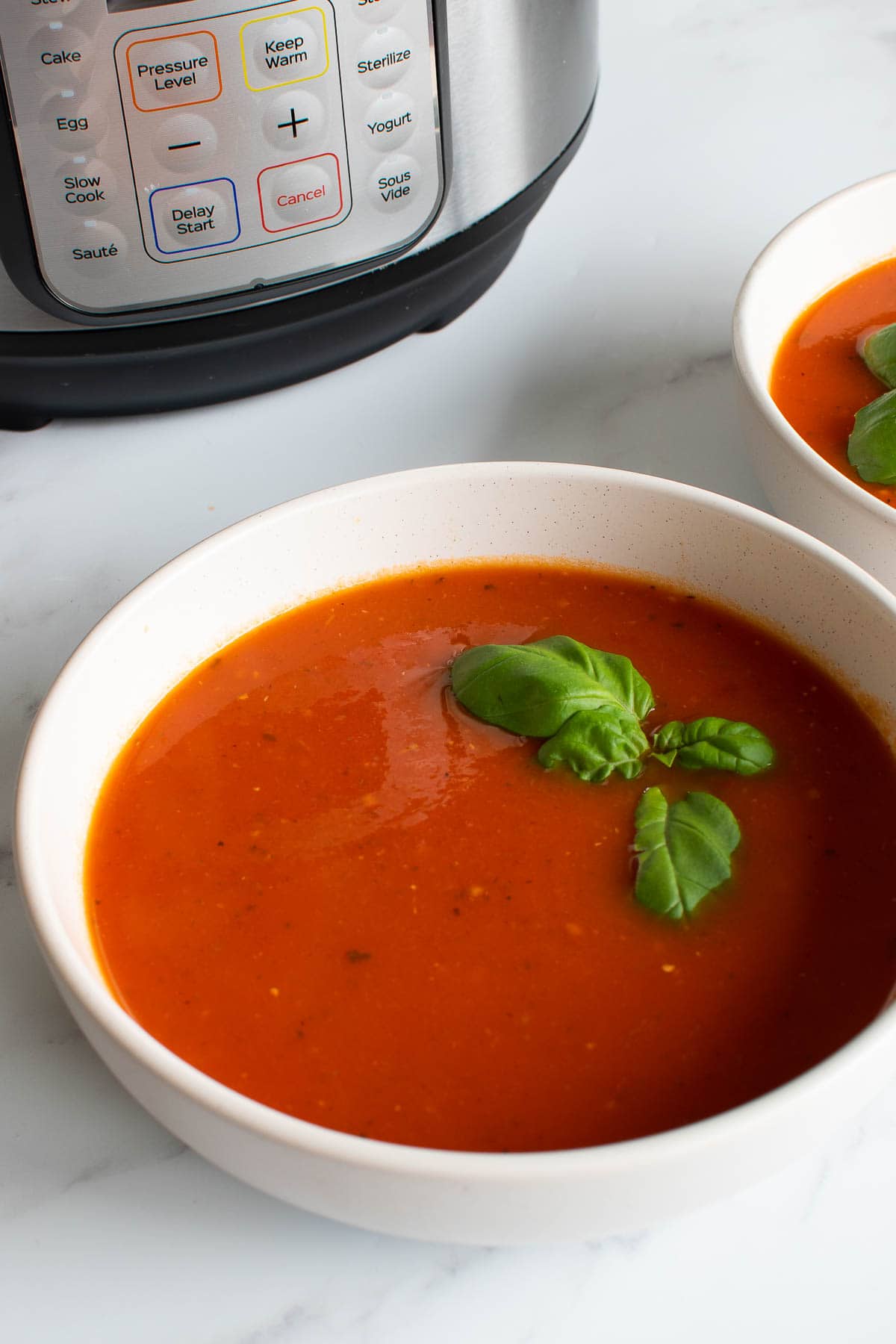 A bowl of tomato soup in front of an Instant Pot.