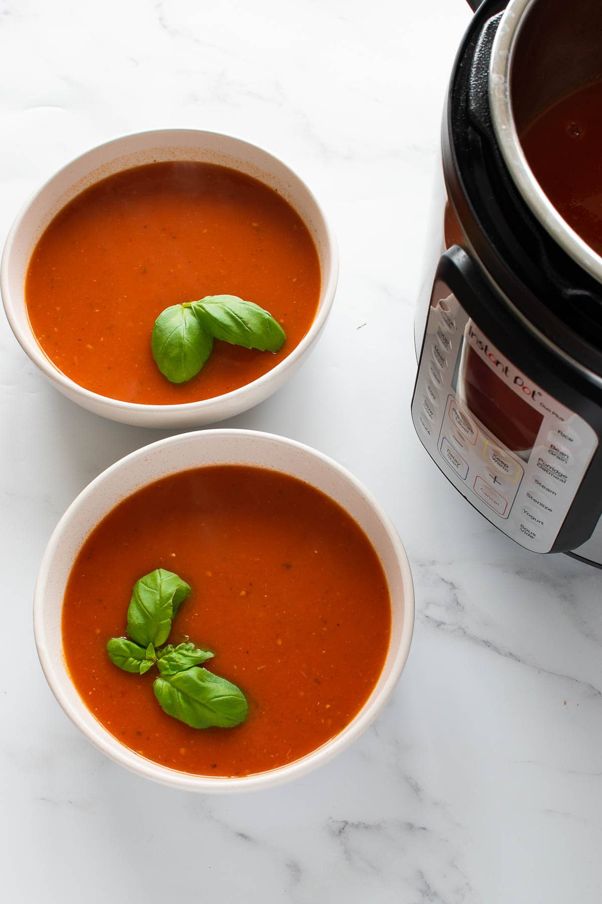 Two bowls of tomato soup with pressure cooker in the background.