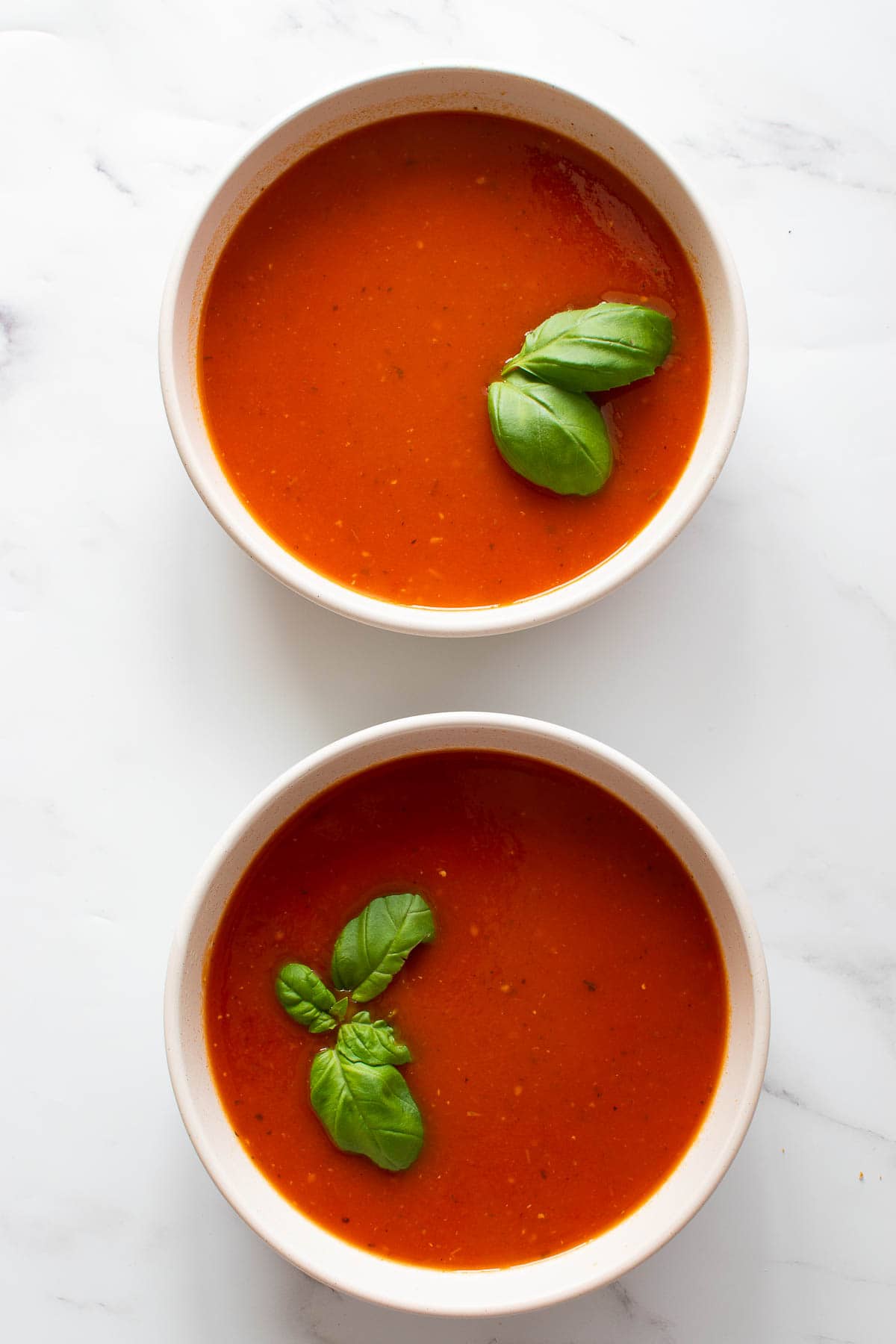 Two bowls of tomato soup with basil.