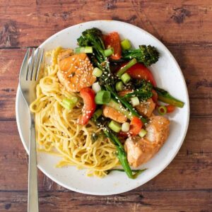 Salmon stir fry on a plate with noodles.