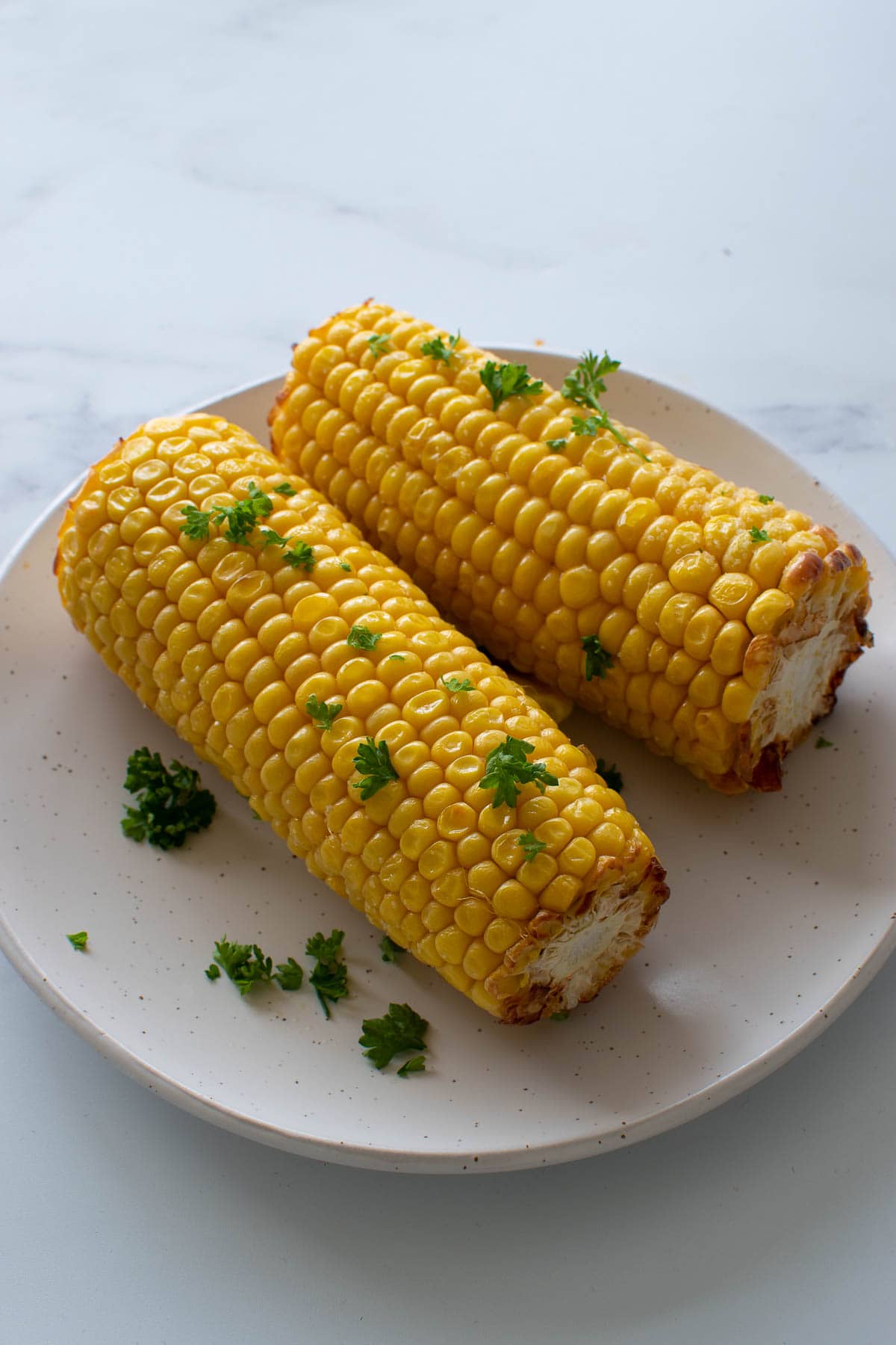 Two cooked cobs of corn on a plate.