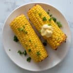 Corn on the cob on a white plate, topped with melting butter.
