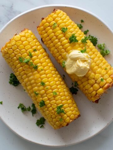 Corn on the cob on a white plate, topped with melting butter.