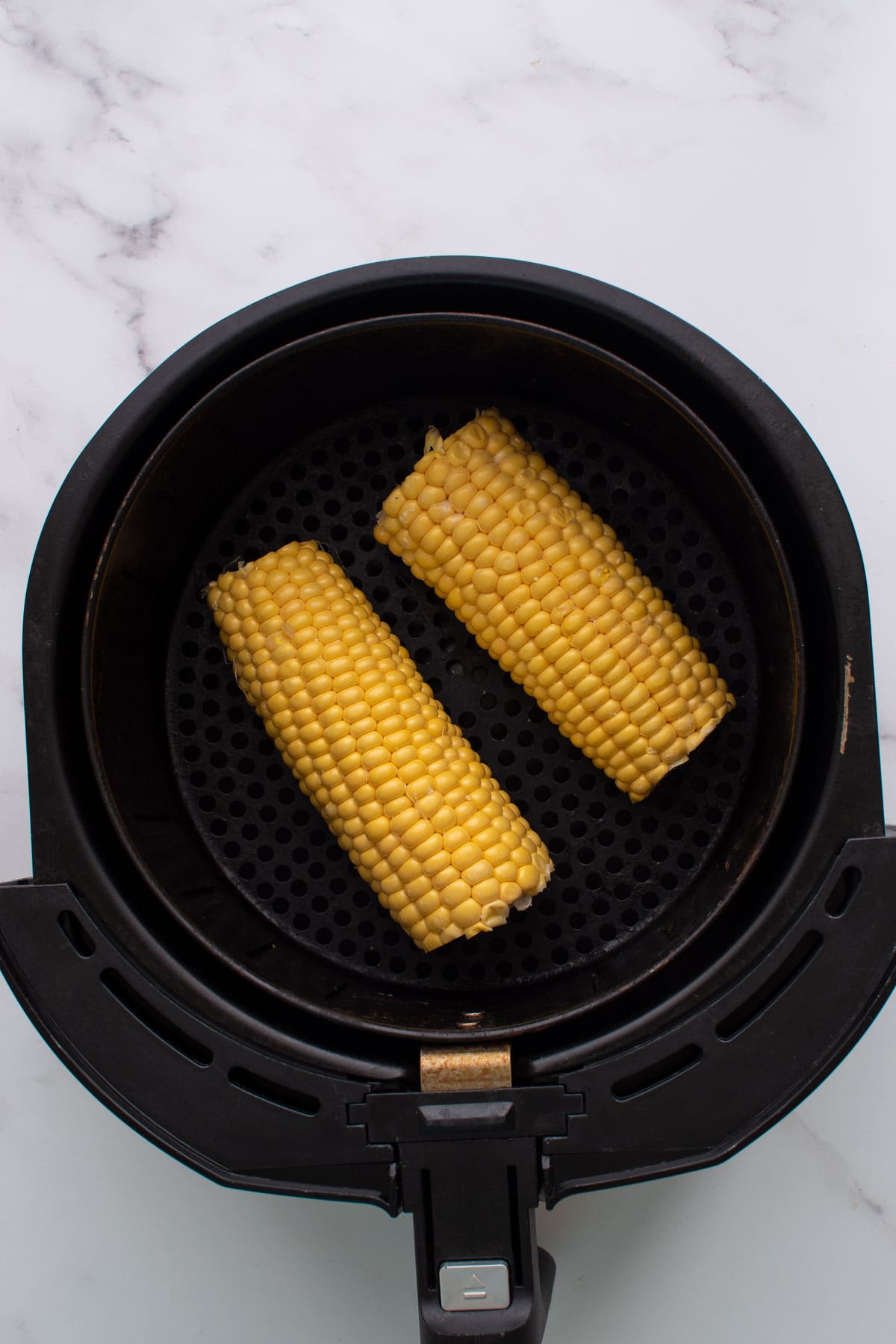 Two cobs of corn in an air fryer.