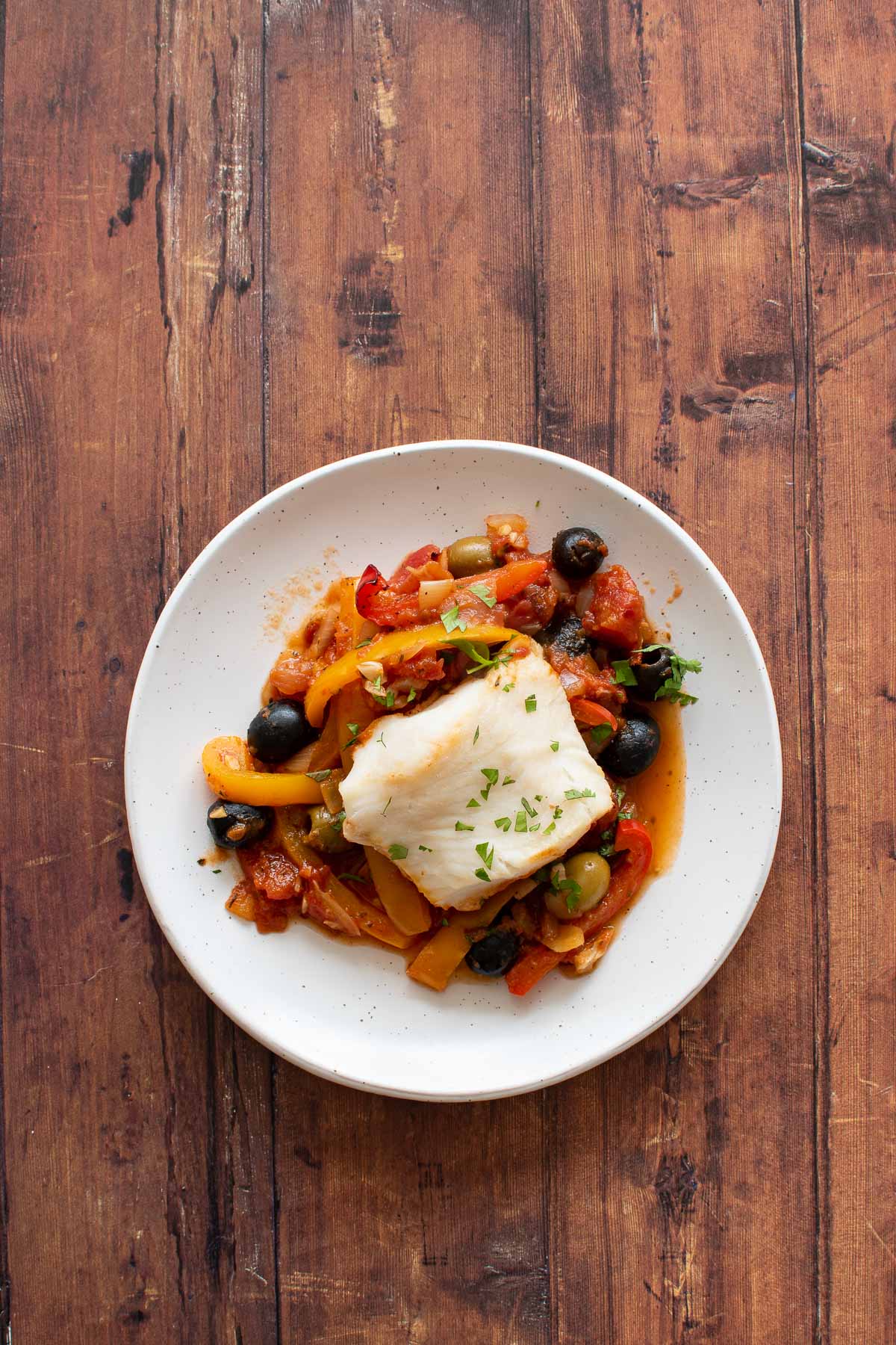 A plate with hake fillets, olives and vegetables.