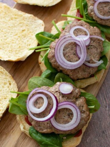 Three baked turkey burgers on a wooden board.