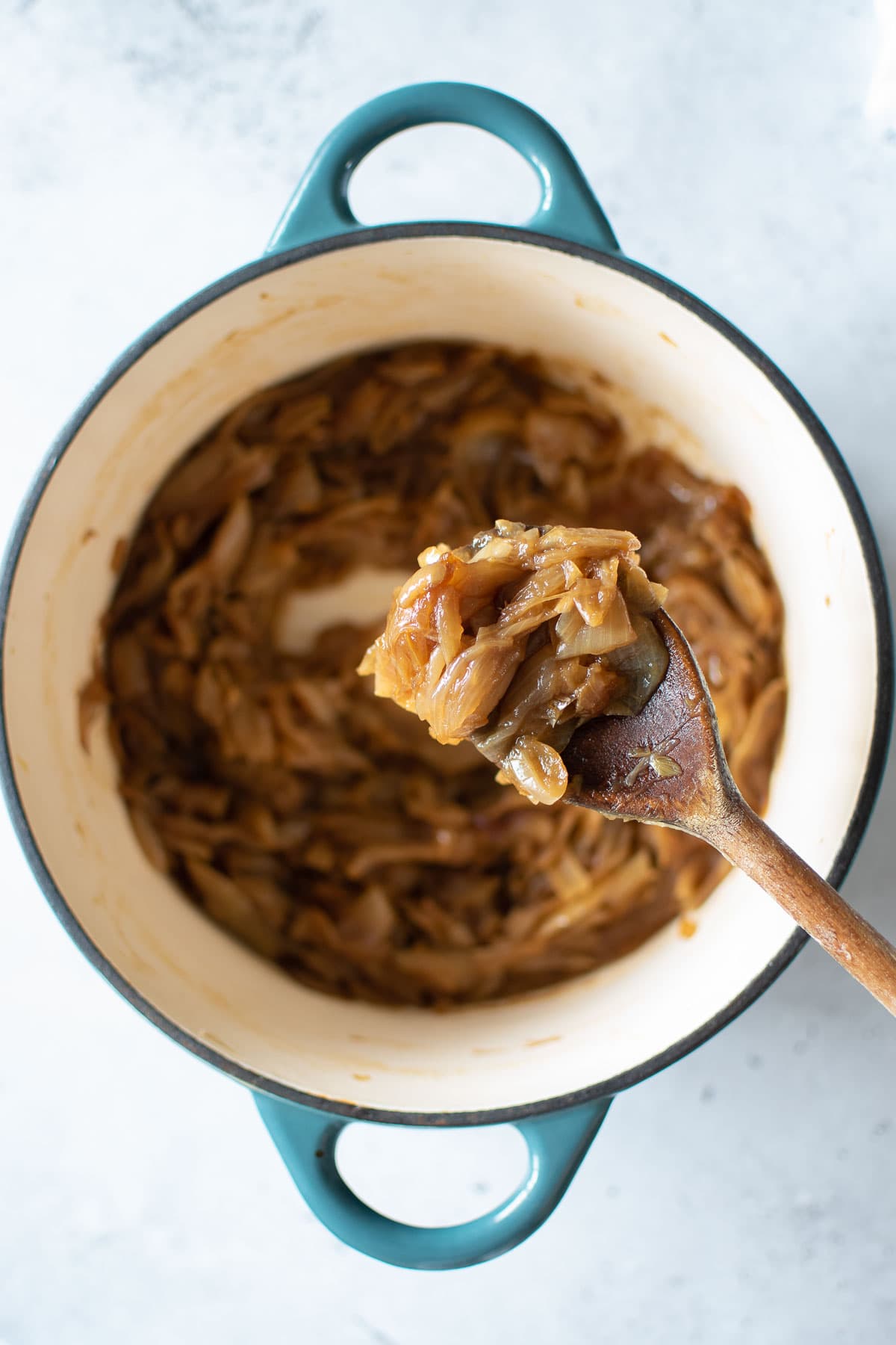 A wooden spoon lifting up some caramelized onions from a pot.