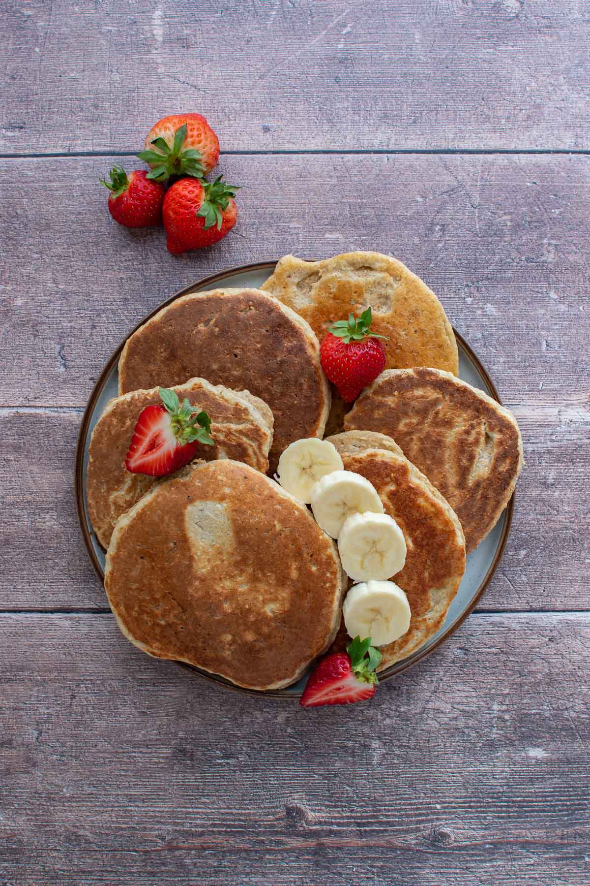 A stack of banana protein pancakes, with strawberries and sliced banana on top.