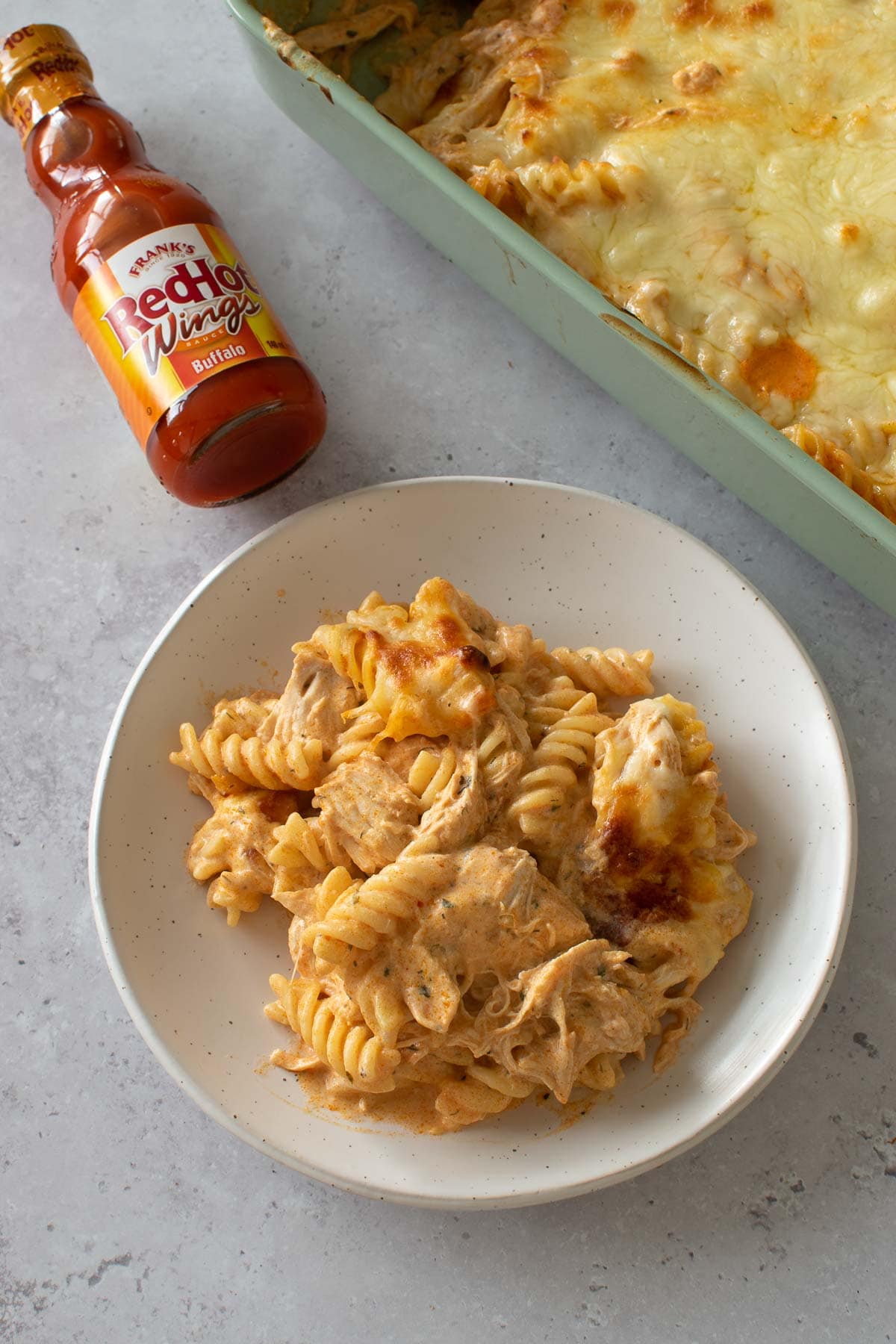 A plate of Buffalo chicken pasta bake with buffalo sauce on the side.