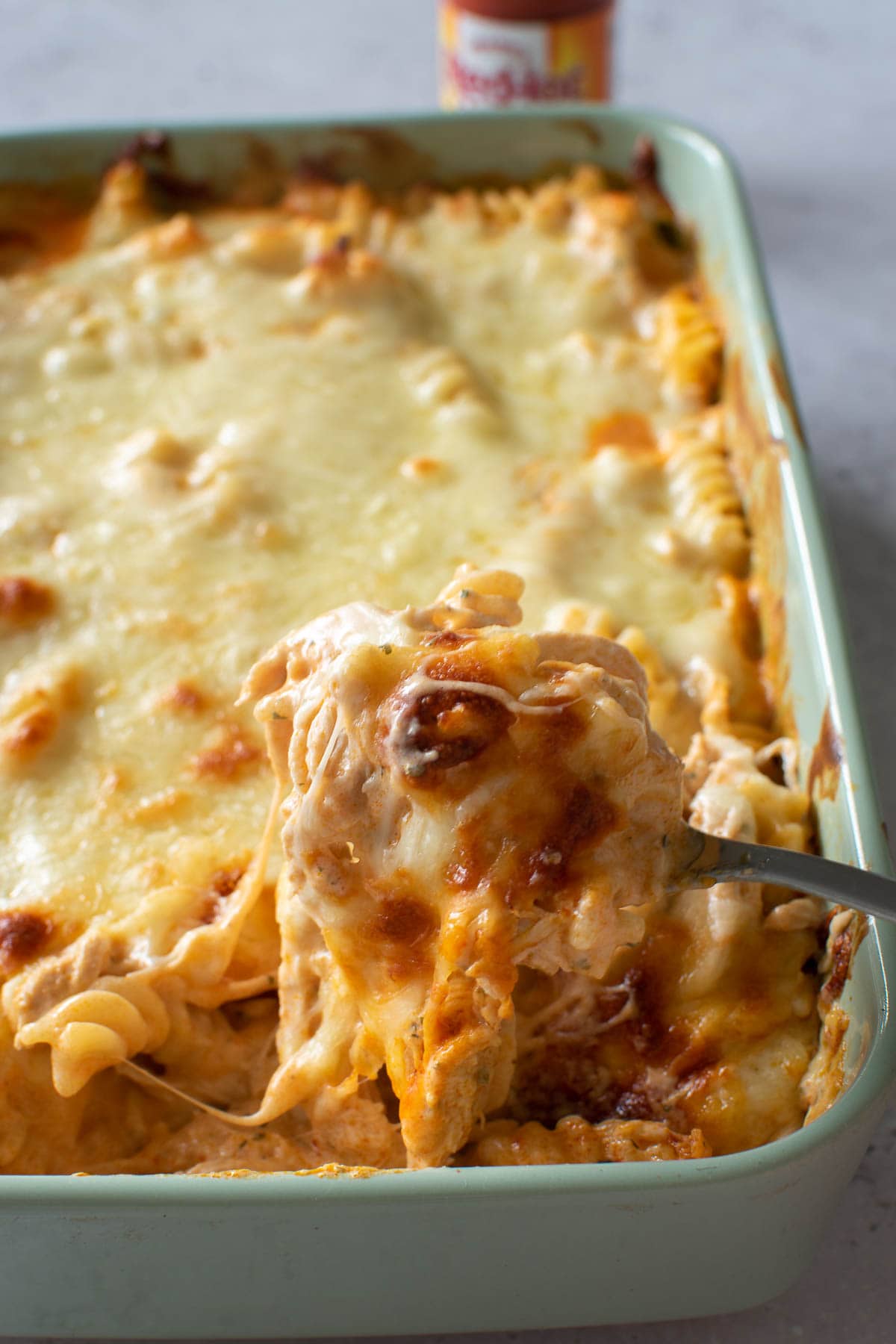 Buffalo chicken pasta bake, with a spoon lifting up a cheesy piece.