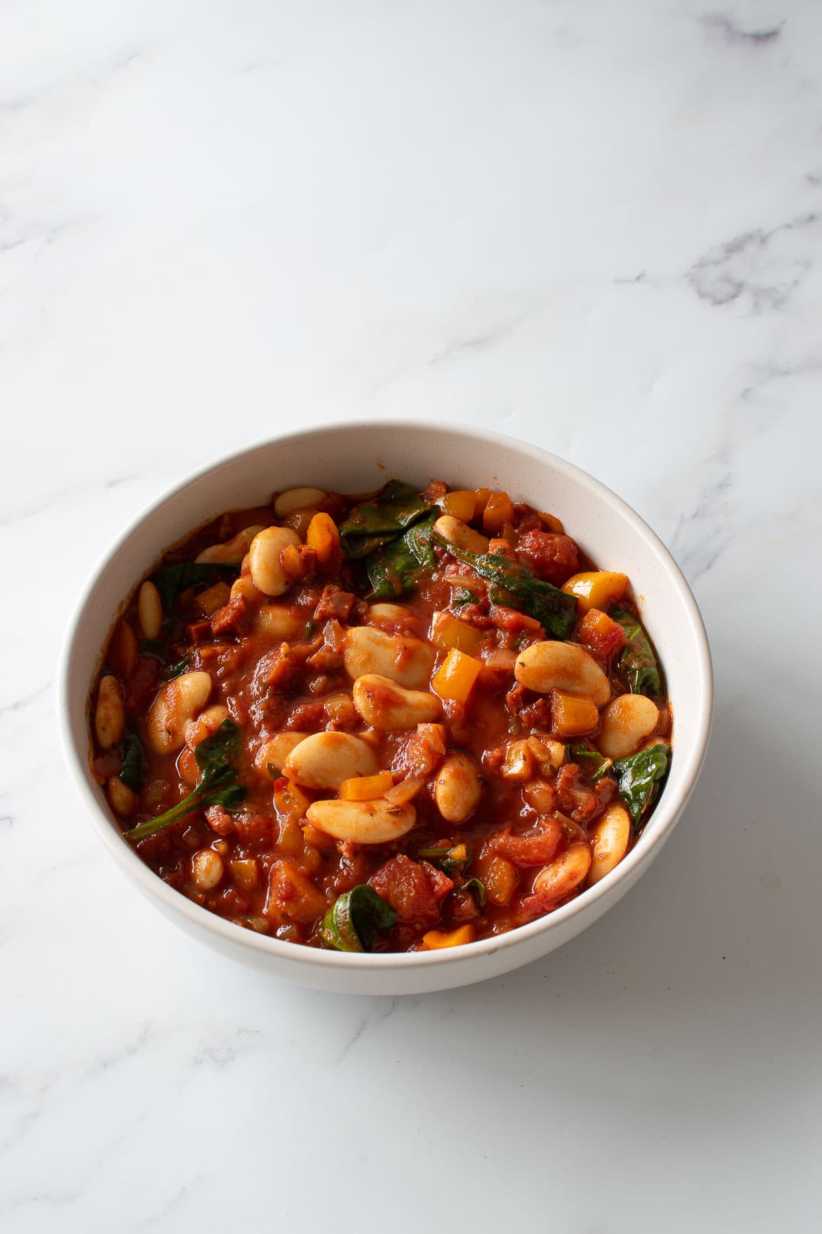 A bowl of stew with chorizo and beans on a table.