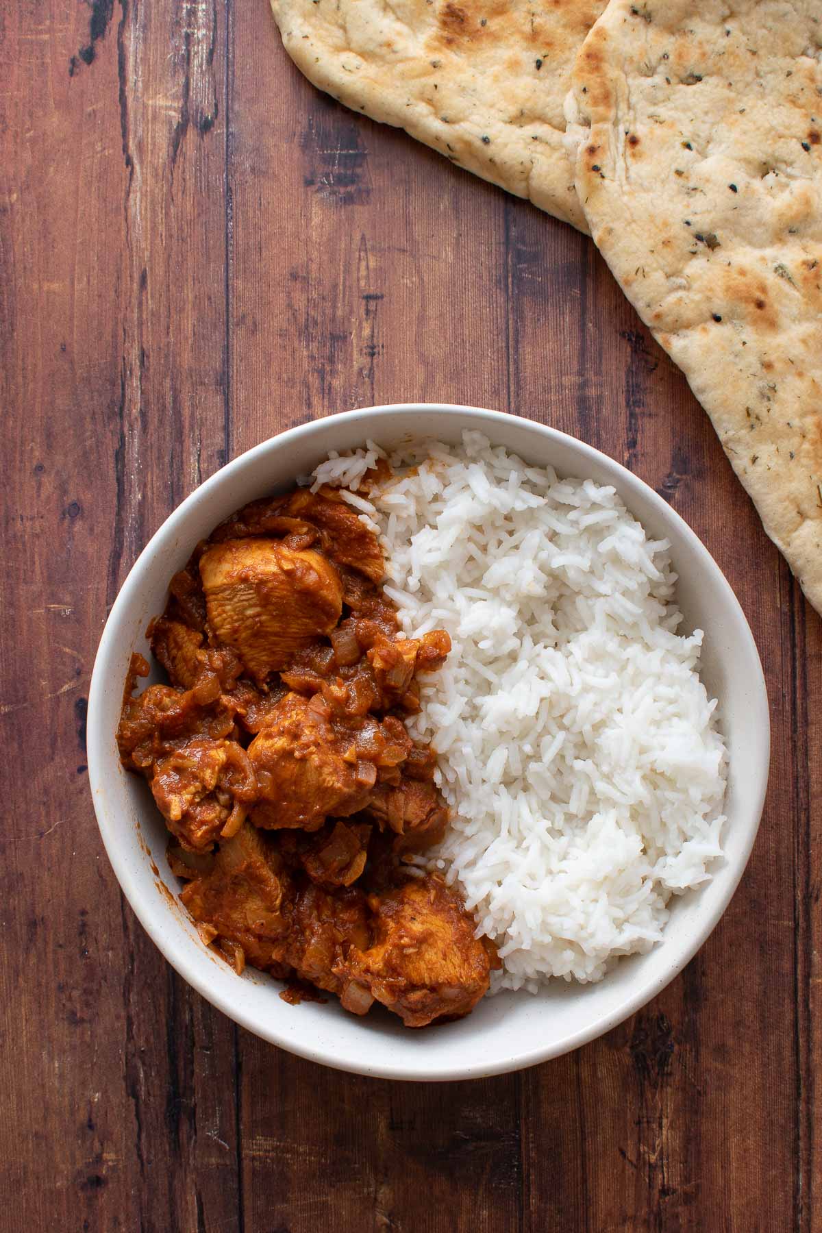 A bowl of chicken rogan josh curry with rice and naan on the side.