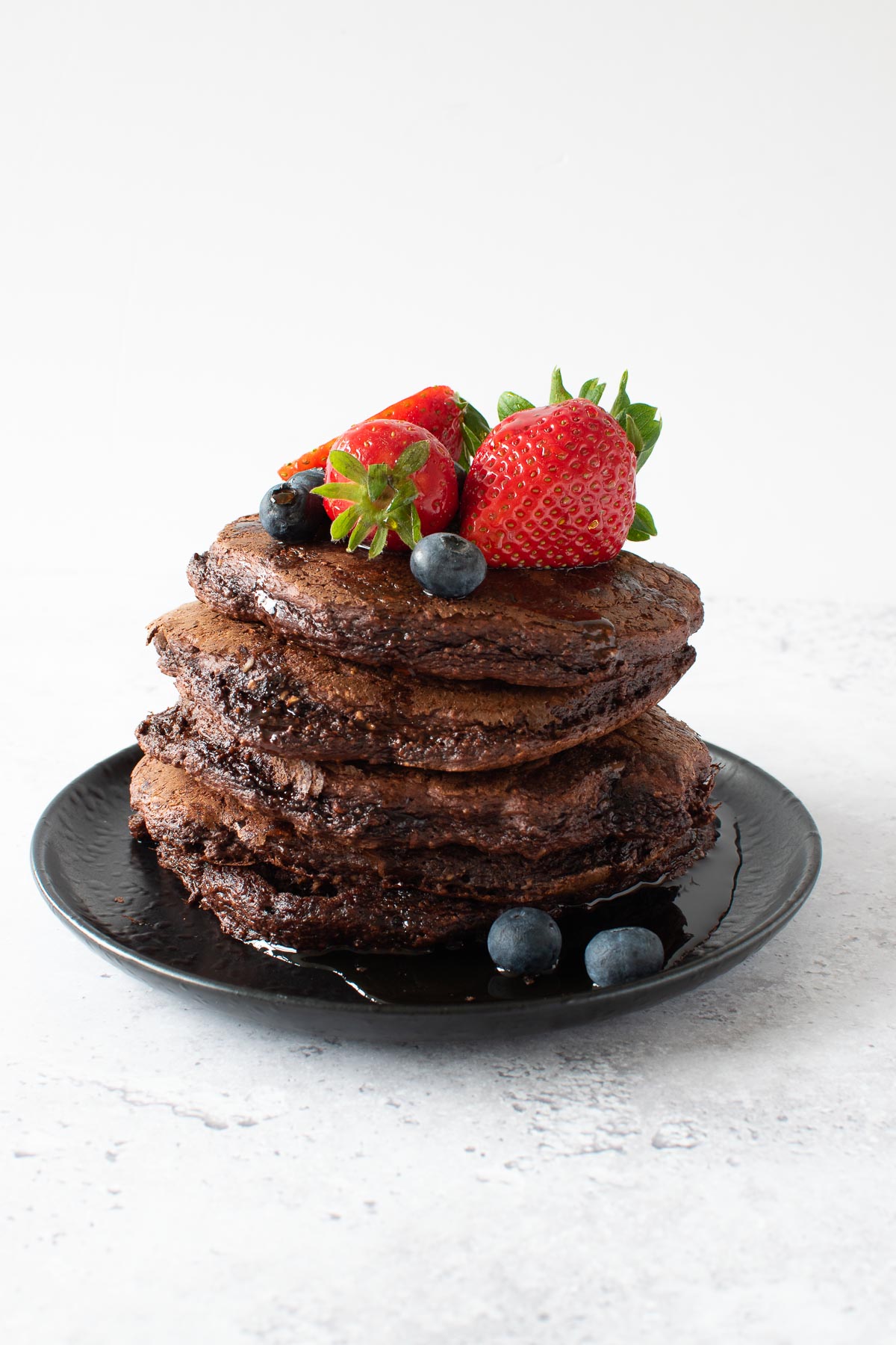 A stack of chocolate protein pancakes with berries on top.