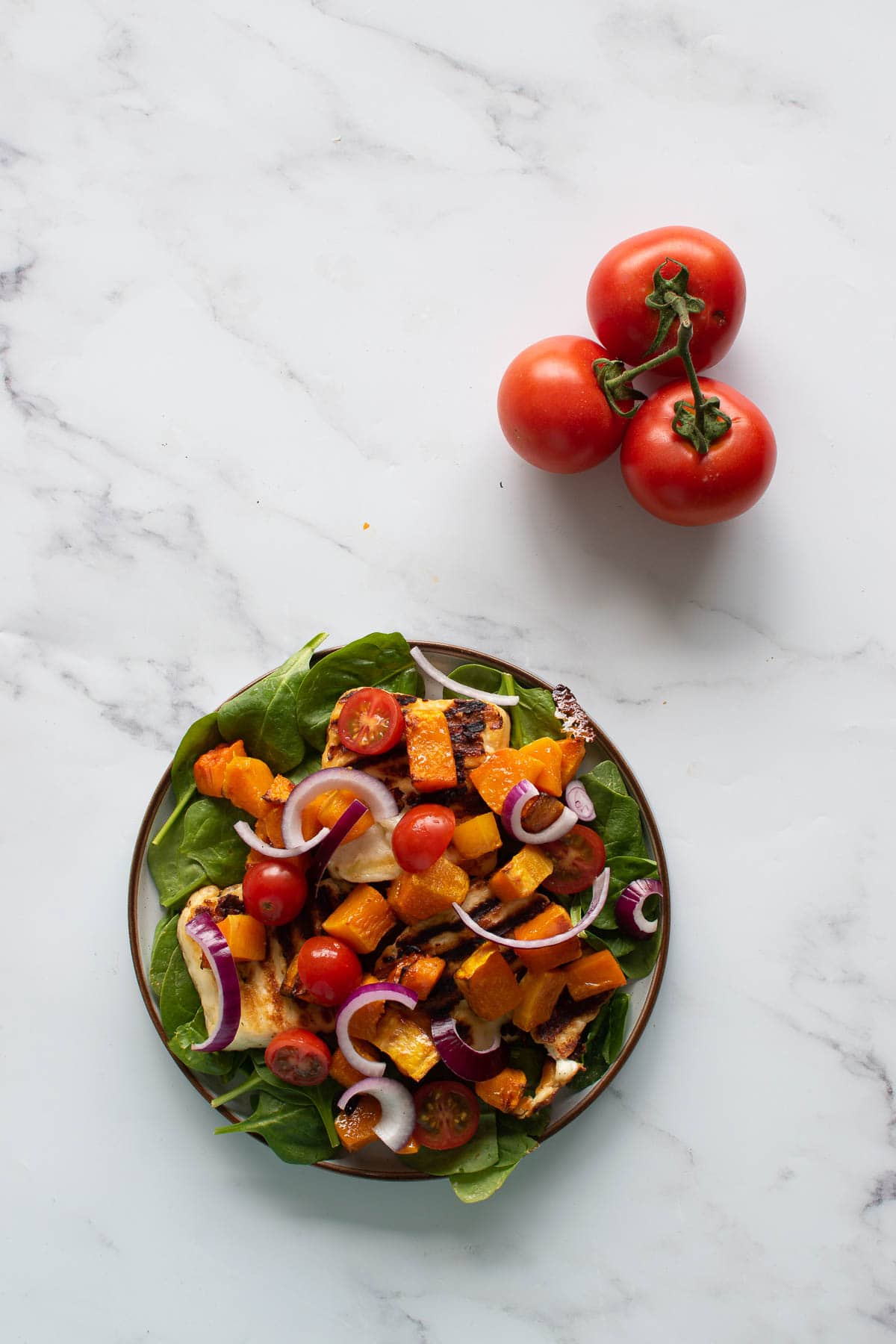 A plate of halloumi salad, with tomatoes on the side.