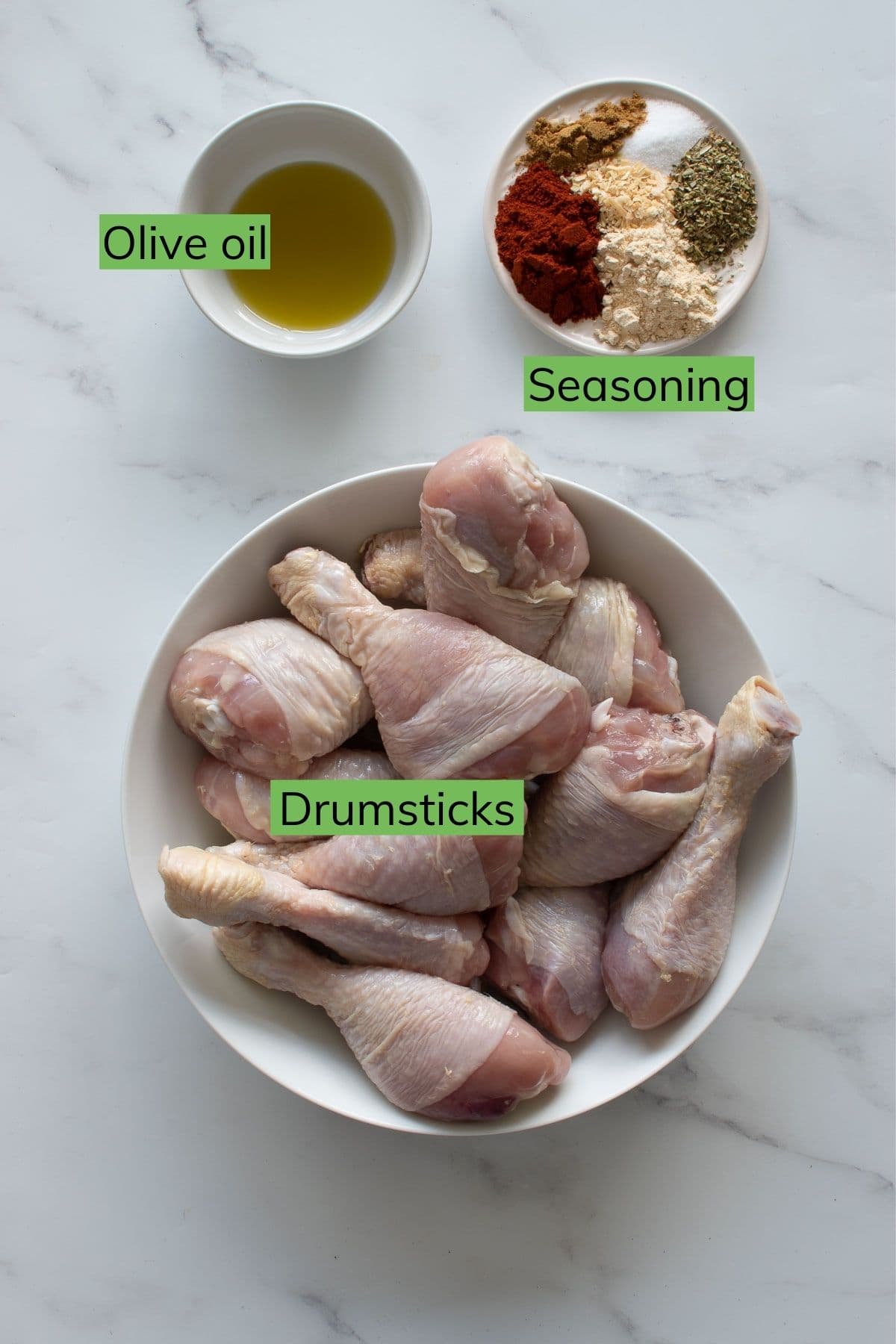 Drumsticks, olive oil and seasoning laid out on a table.