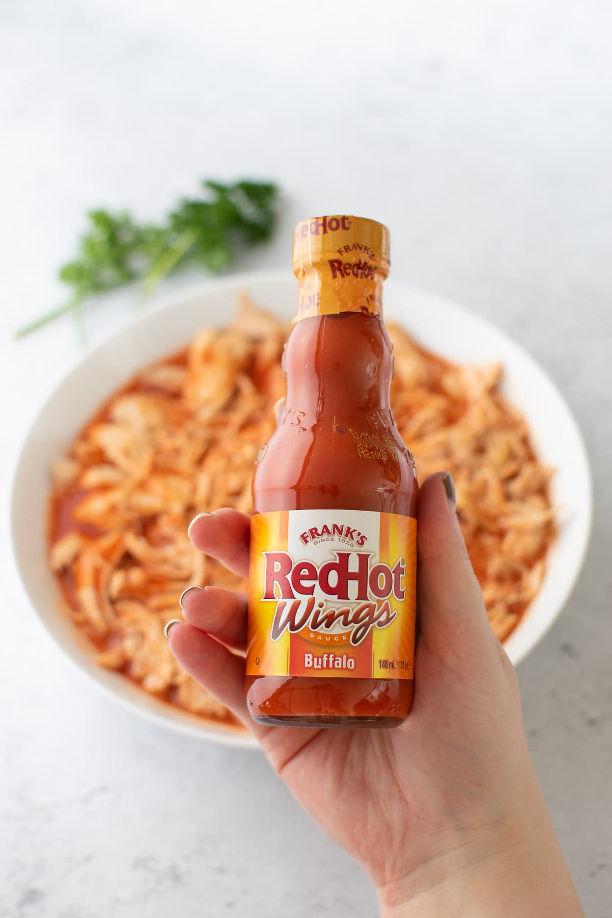 Holding up buffalo sauce in front of a bowl of buffalo chicken.