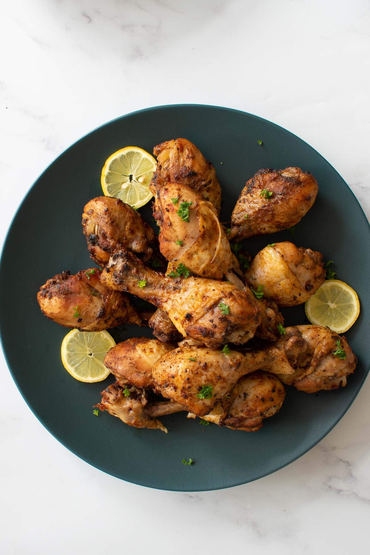 A plate of pressure cooked chicken drumsticks, with parsley and lemon slices.