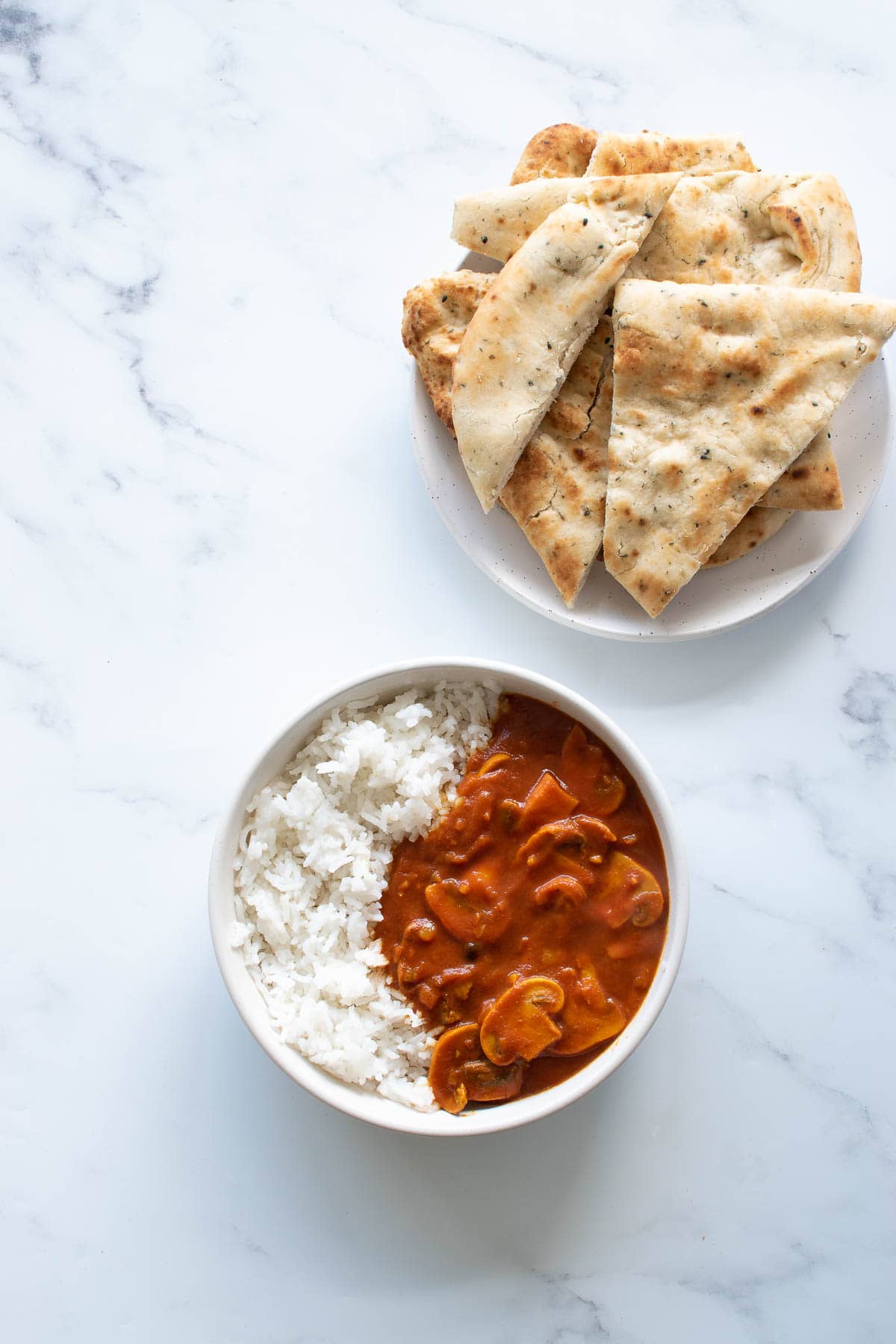 A bowl of curry with rice, and a plate of naan on the side.