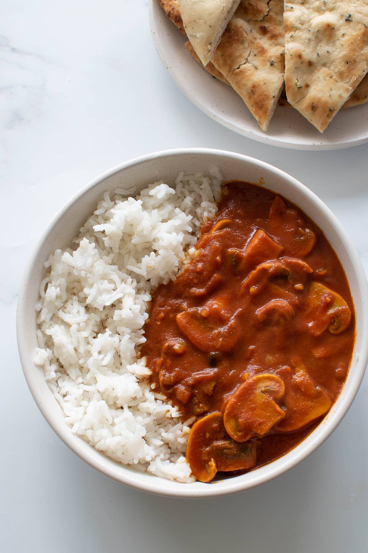 A bowl of mushroom curry with rice, and naan on the side.