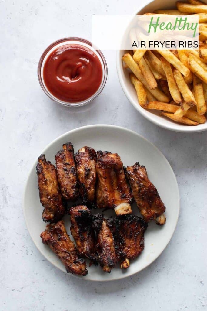 A plate of ribs, with ketchup and fries on the side.