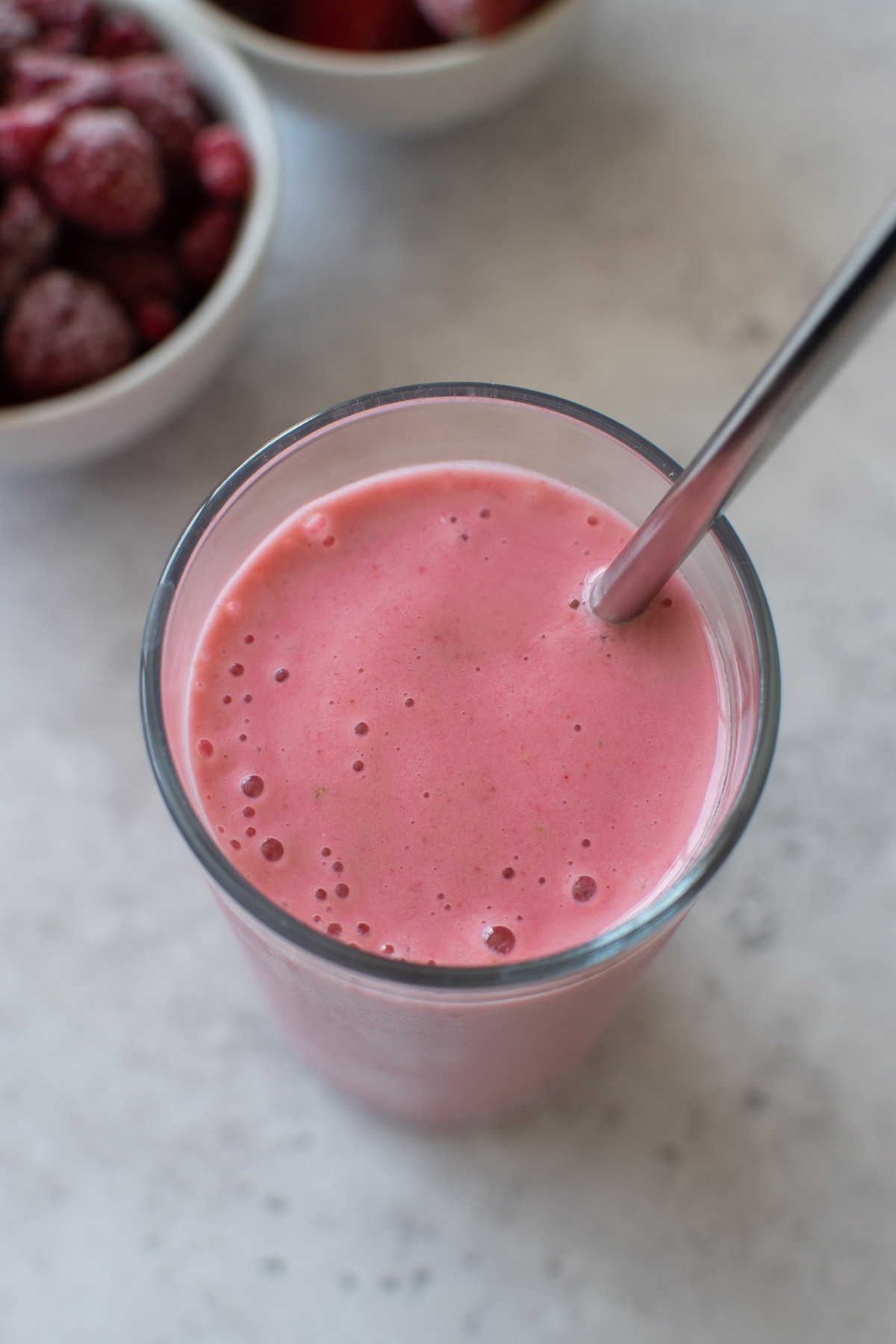 A glass of pink smoothie with a metal straw.