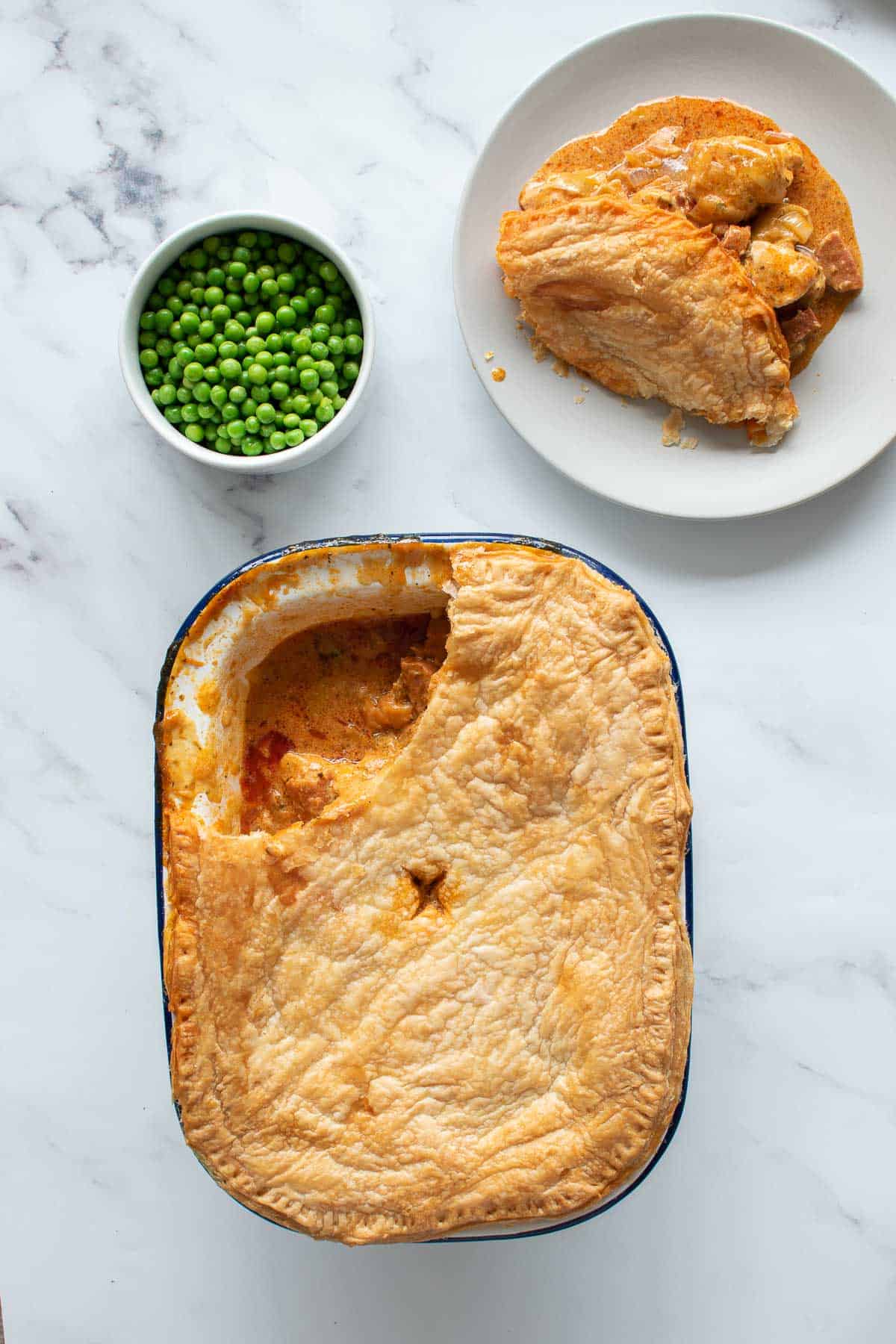 Pie with chicken and chorizo, with a serving placed onto a plate and a bowl of peas on the side.