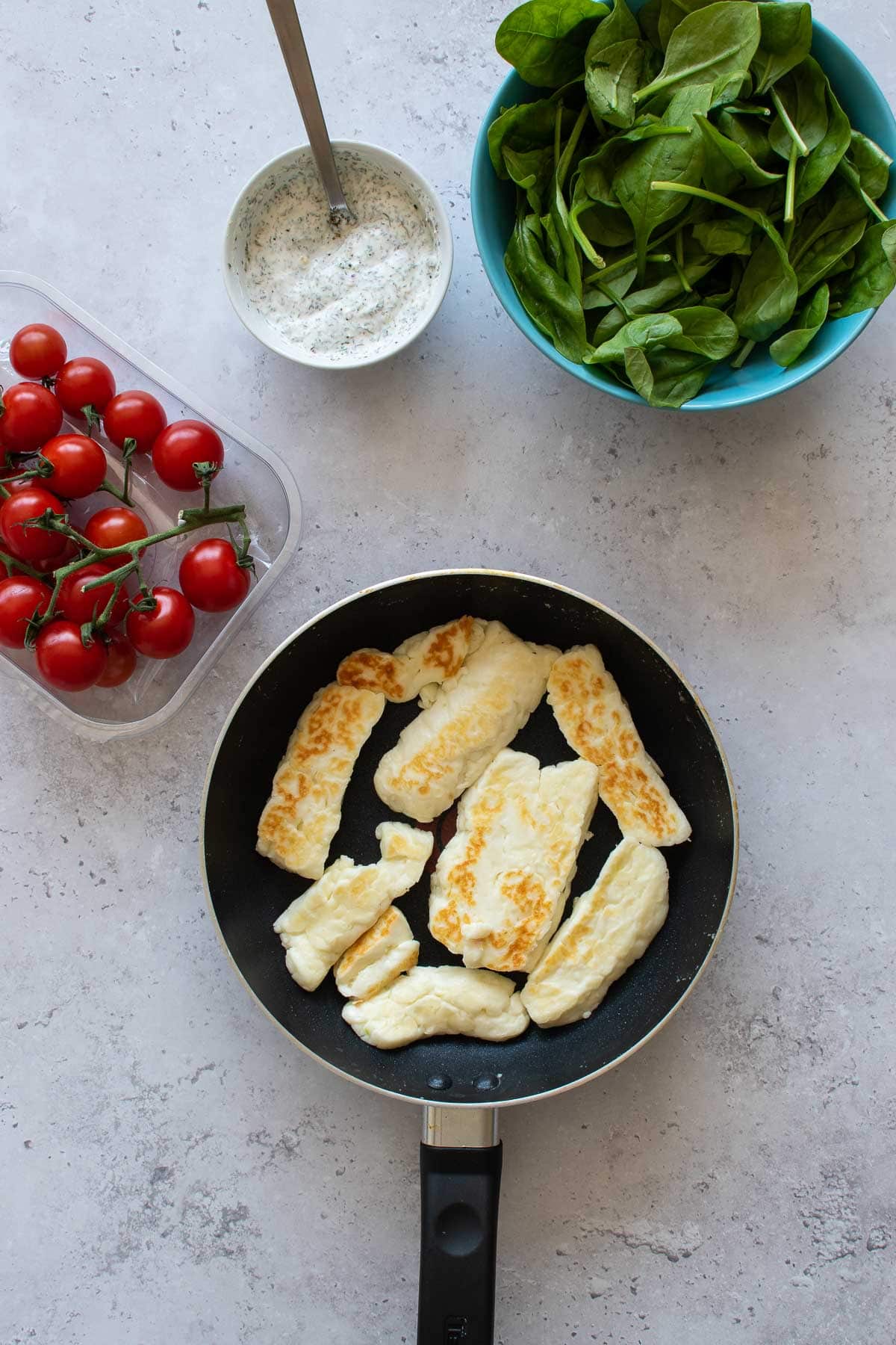 Grilled halloumi in a pan, with tomatoes, spinach and tzatziki on the side.