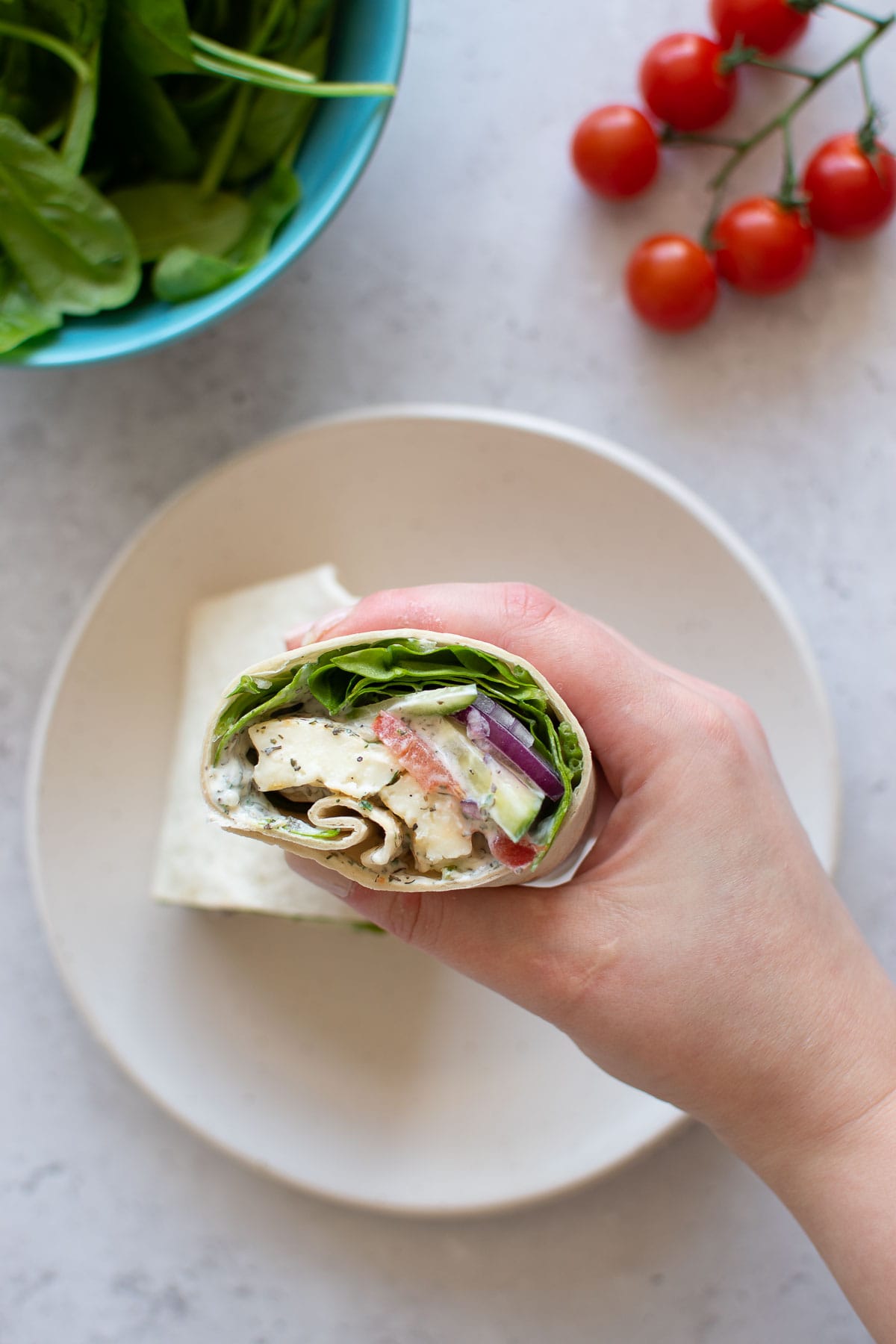 A hand holding a wrap with halloumi and spinach.