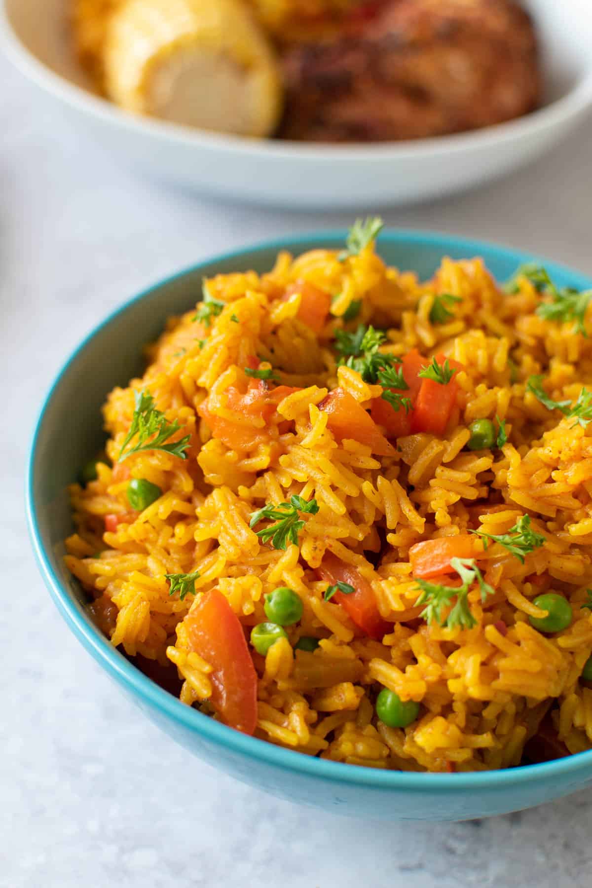 A blue bowl filled with spicy rice. Corn on the cob and chicken in the background.