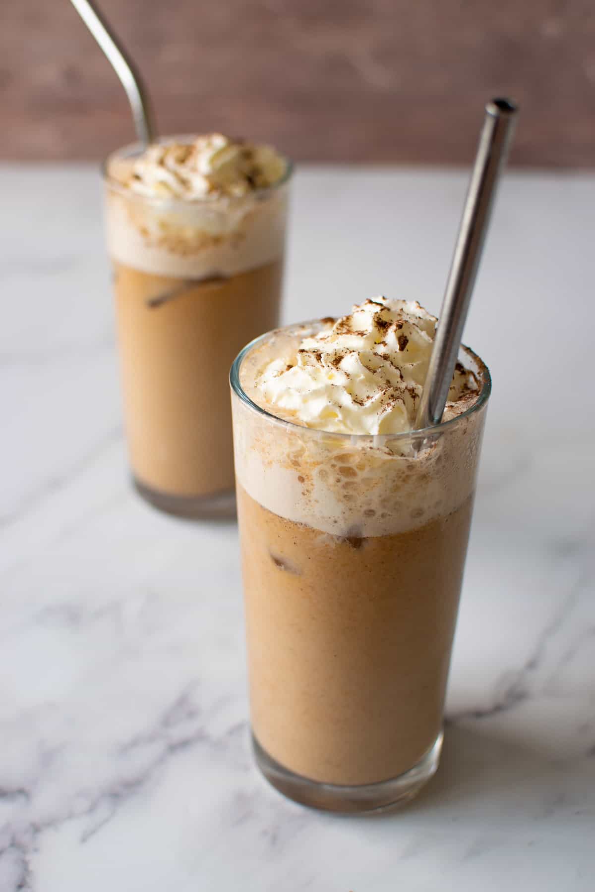 Two classes of iced pumpkin latte with whipped cream. Metal straws added.