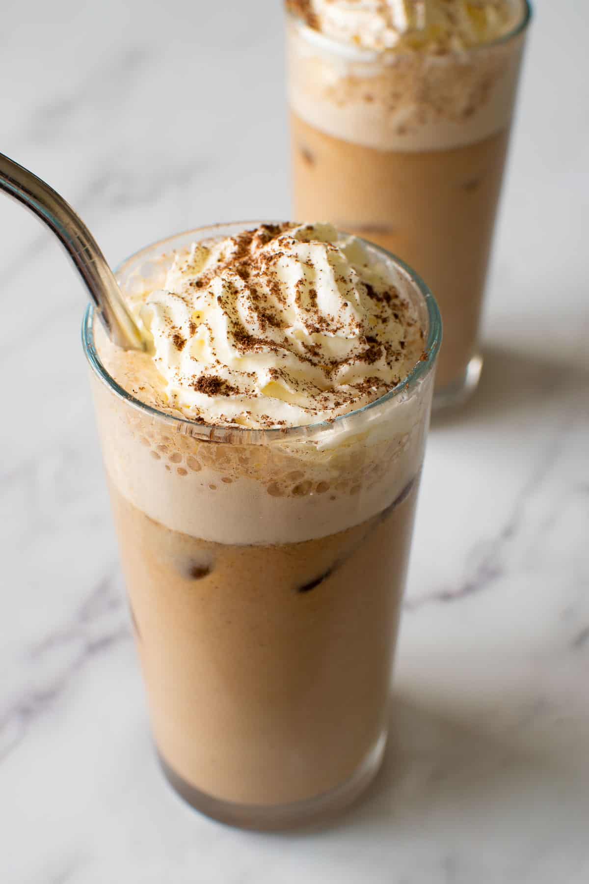 Close up of a glass with iced pumpkin spice latte and whipped cream.