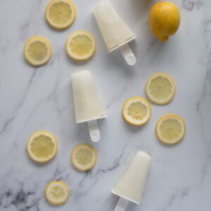 Three lemonade popsicles on a table, surrounded by lemon slices.
