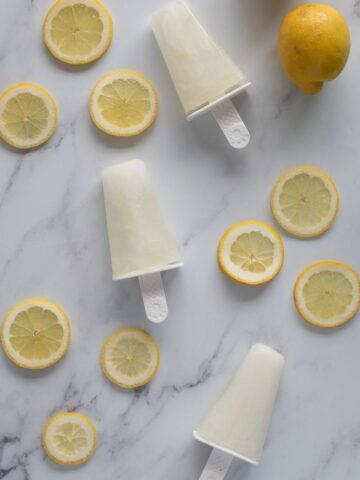 Three lemonade popsicles on a table, surrounded by lemon slices.