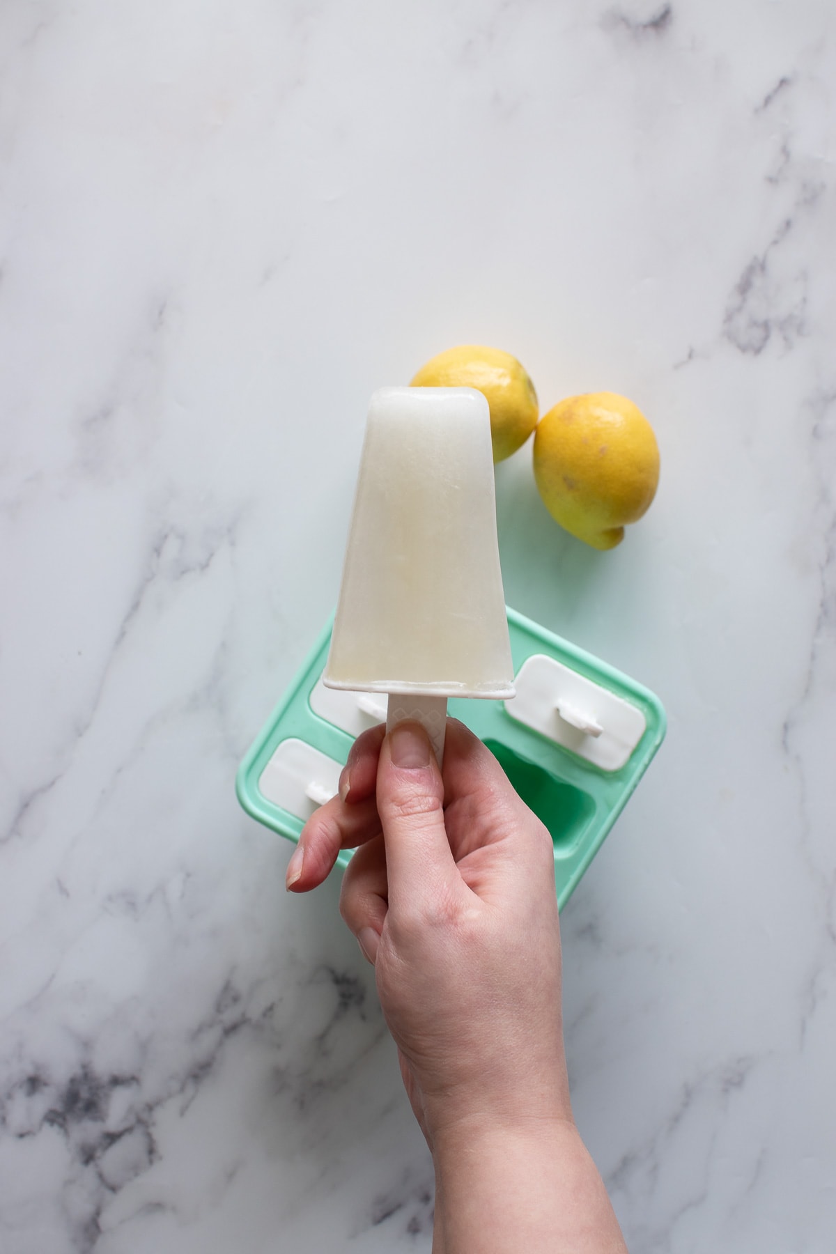 A hand holding a lemon popsicle.