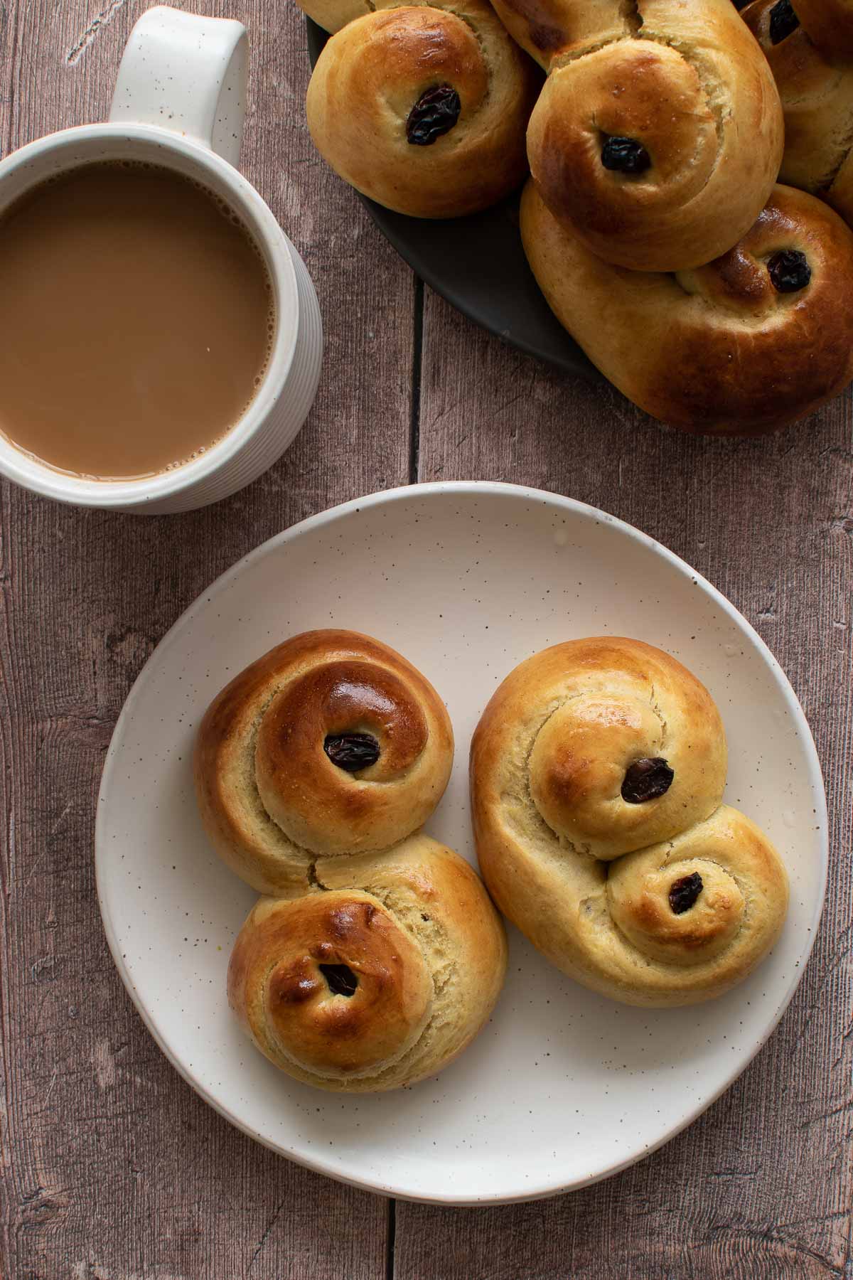 Lussekatter on a plate, with a cup of coffee on the side.