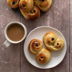 Lussekatter on a plate, with a cup of coffee on the side.